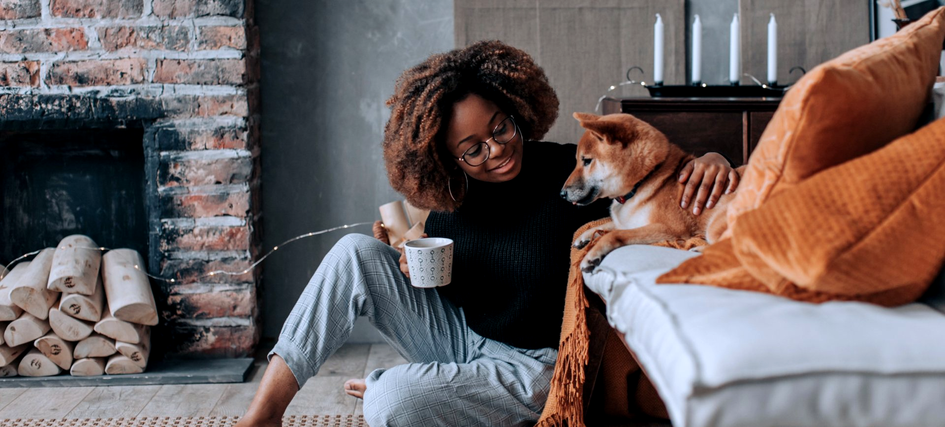A woman is sitting on the floor with a dog and a cup of coffee.