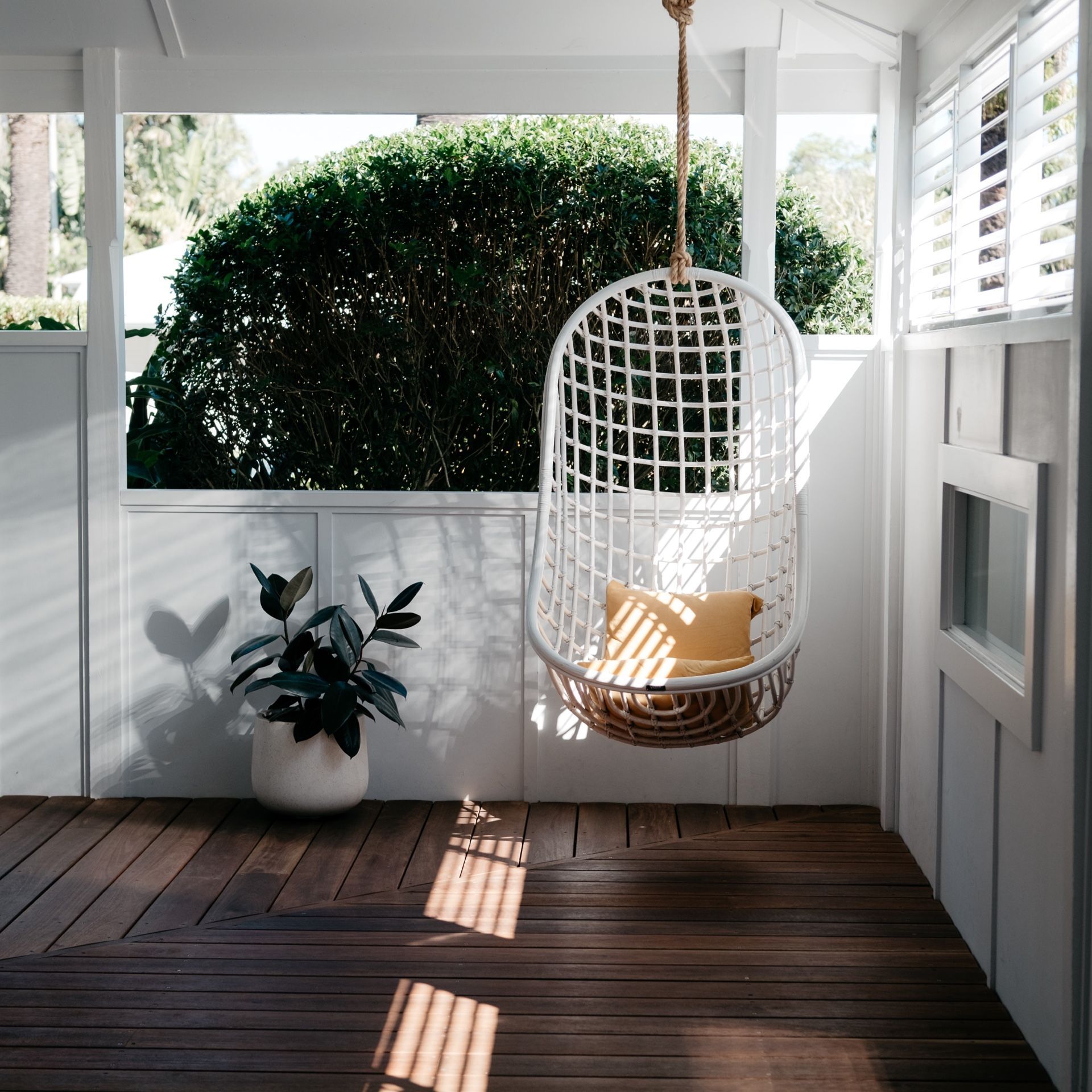 A hanging chair with a yellow pillow is sitting on a wooden deck.