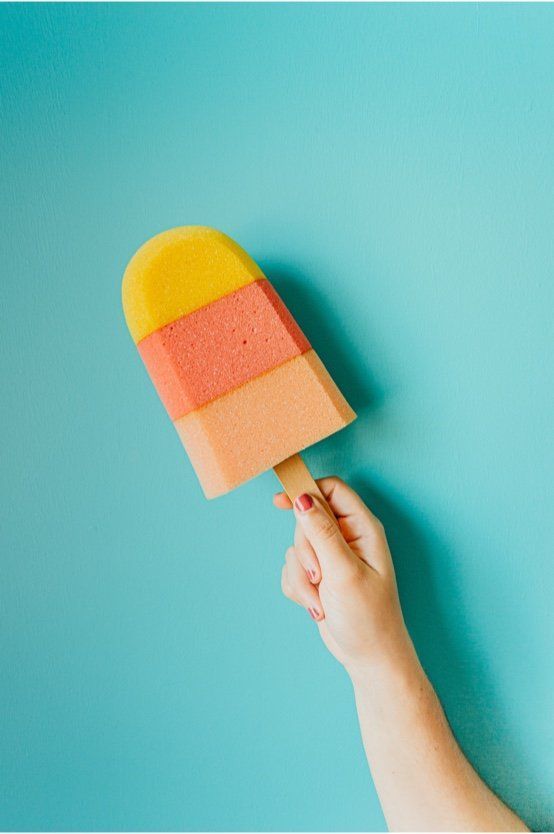 Hand holding a yellow, coral, and peach popsicle on a turquoise background
