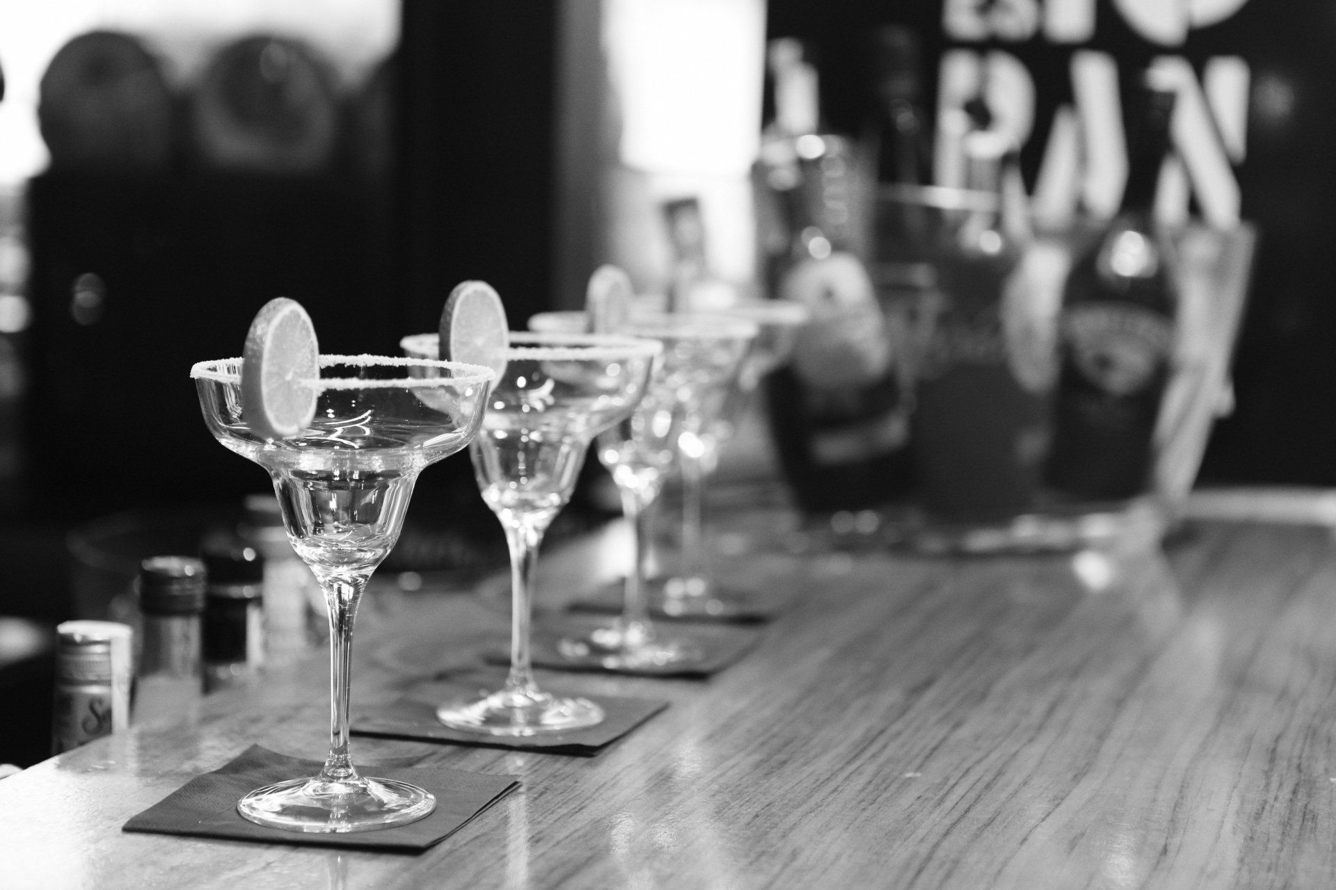 A black and white photo of a row of martini glasses on a bar.