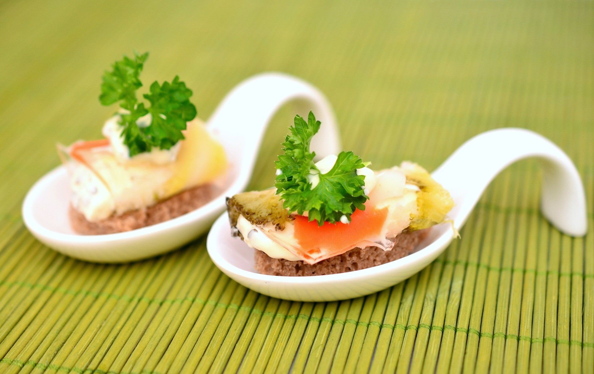Two white spoons filled with food on a green mat