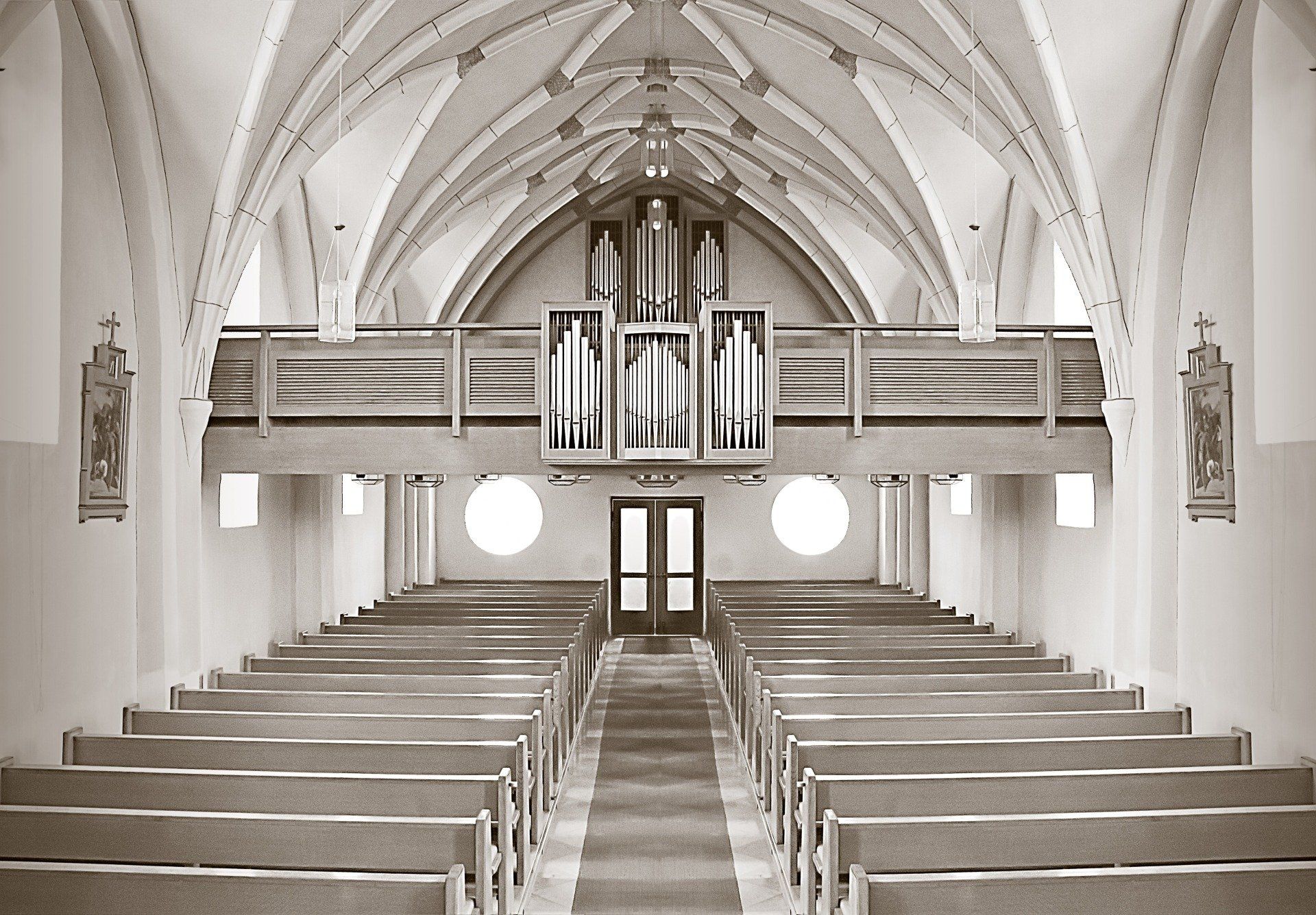 Interior view of a church. Rows of wooden pews face a central aisle leading to an organ and a doorway.