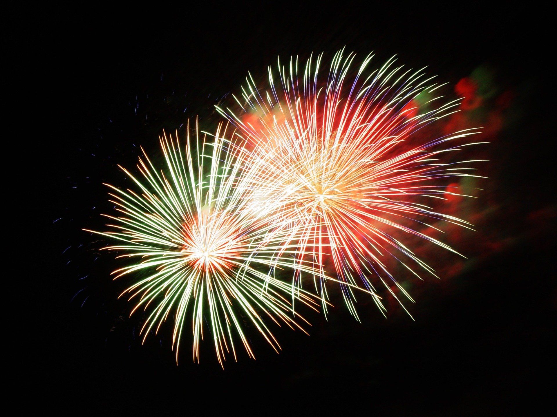 Red and green fireworks are exploding in the night sky