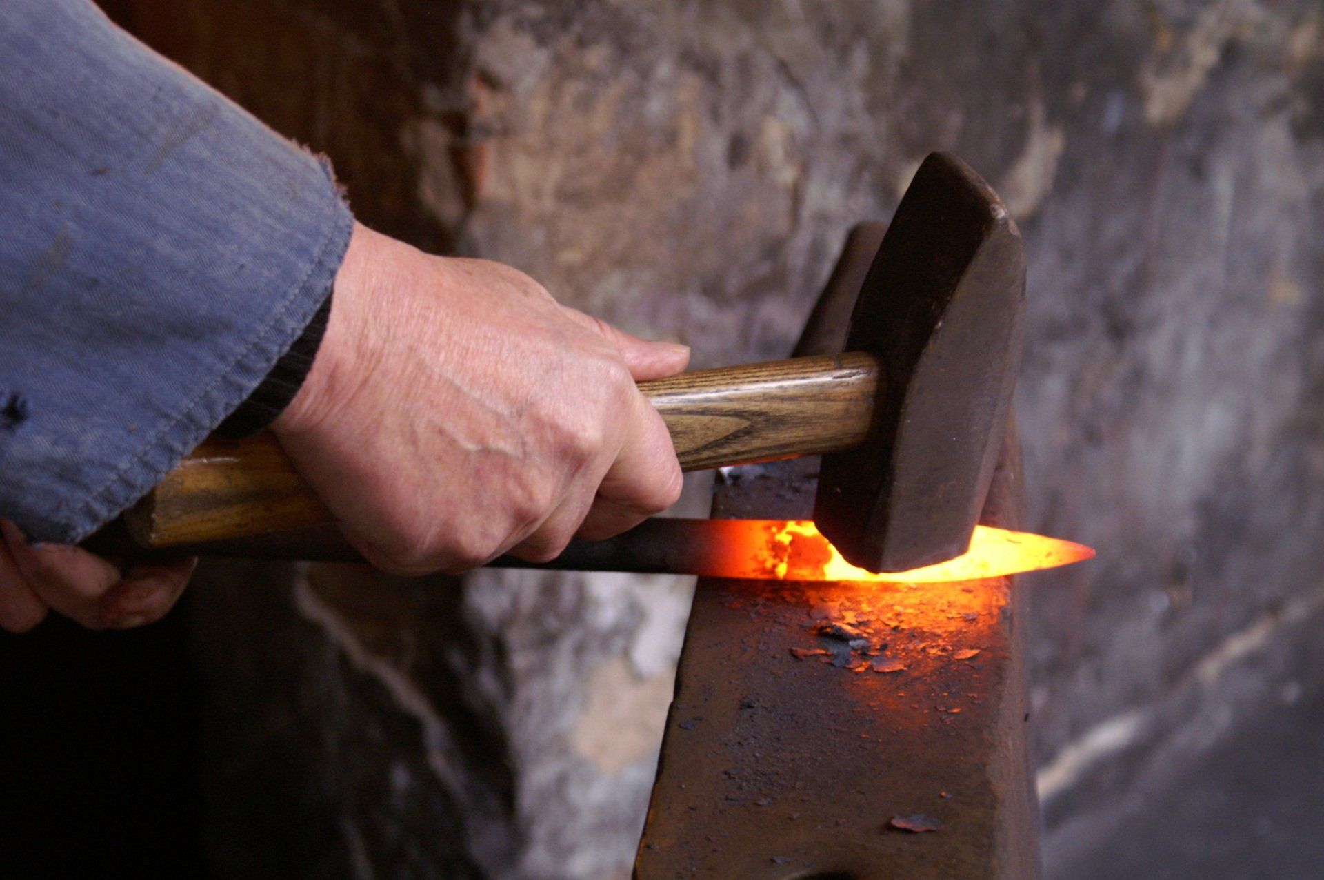 A person is holding a hammer over a piece of hot metal.