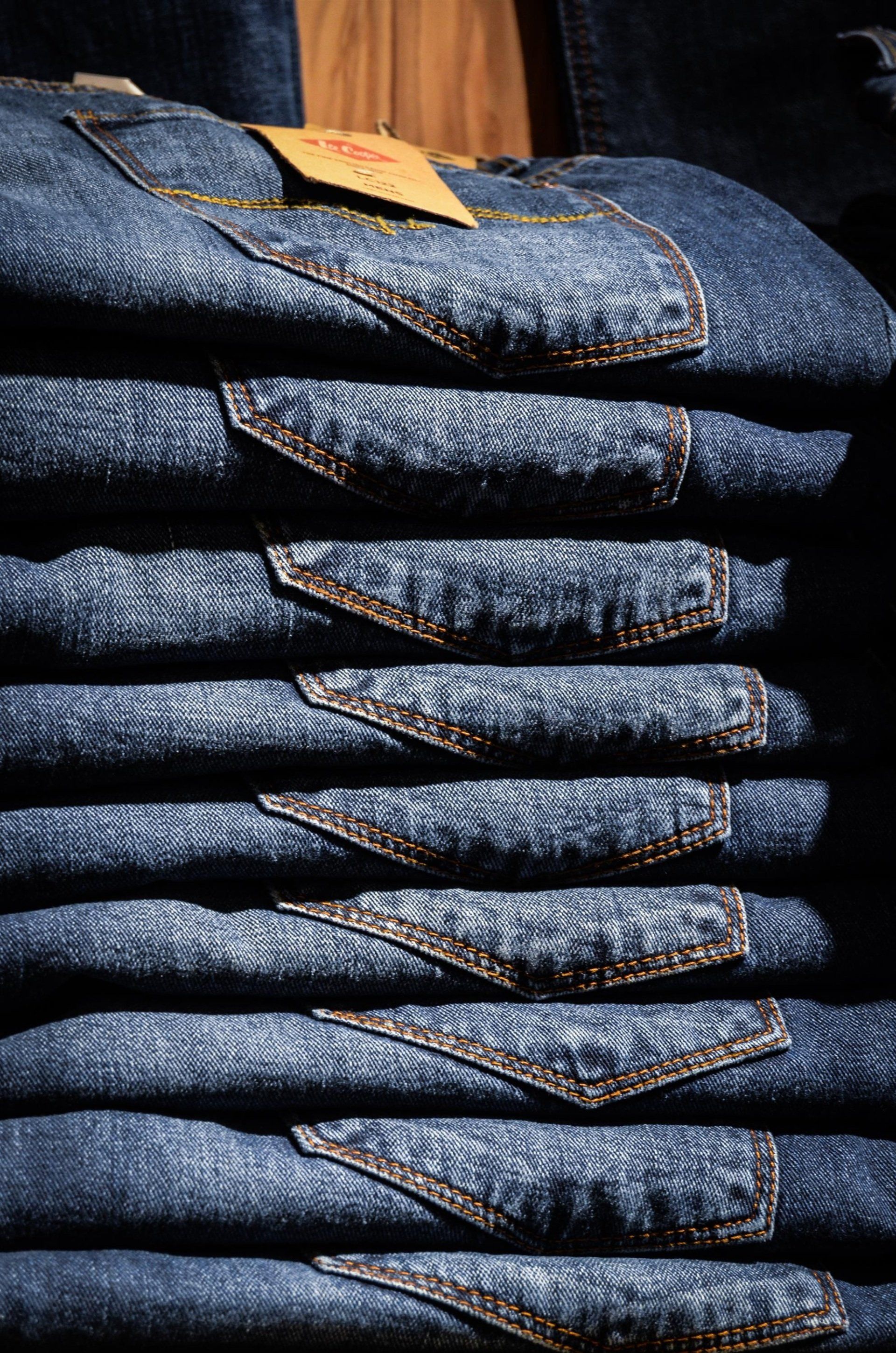 A vertical stack of folded dark blue denim jeans, with a yellow tag visible on the top pair.