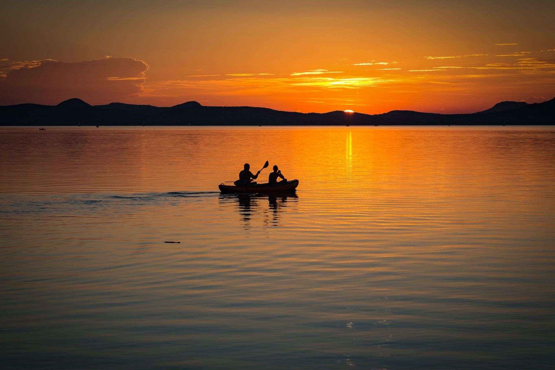 Two people are in a kayak on a lake at sunset.