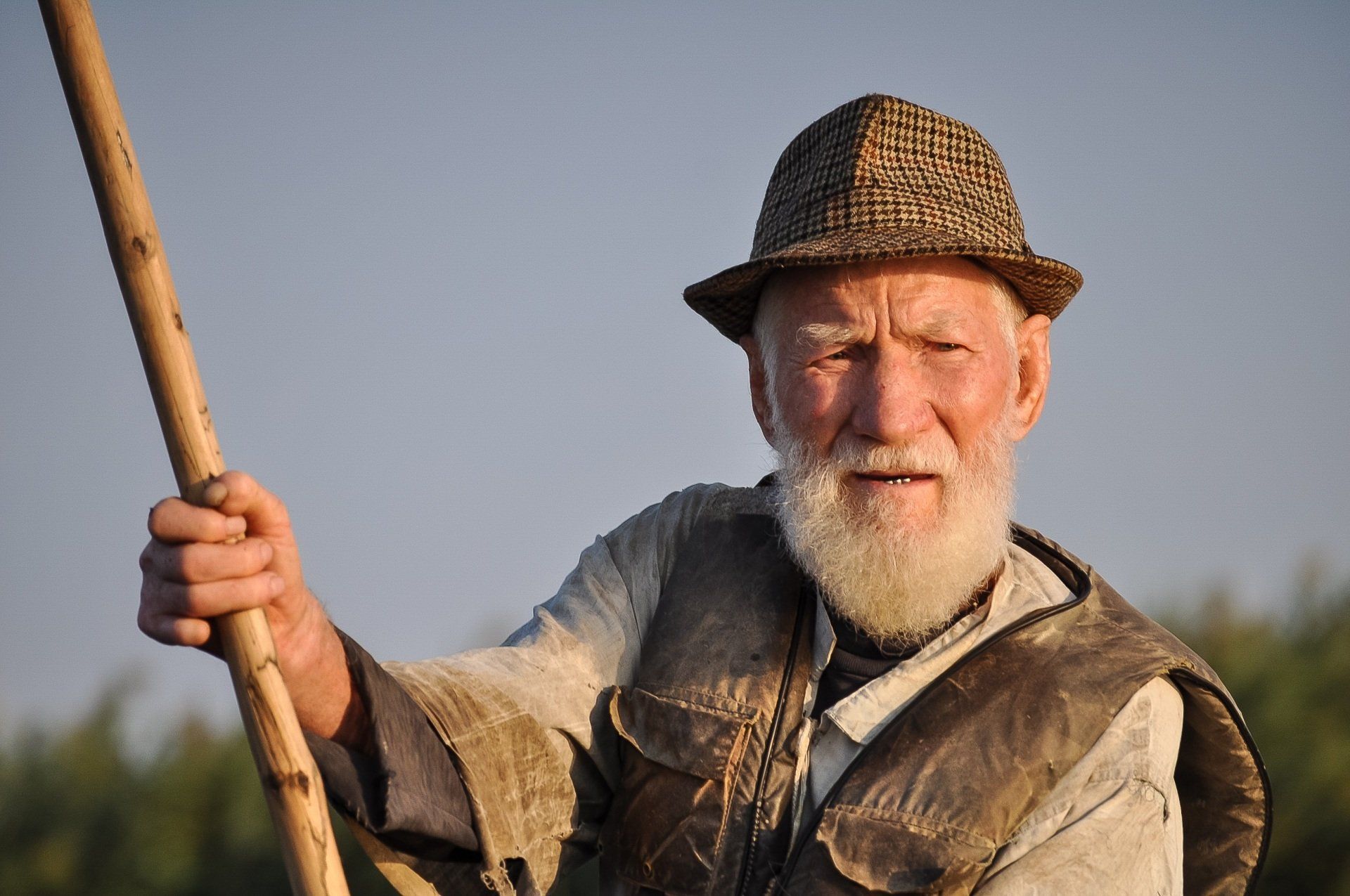 A man with a beard and hat is holding a wooden stick.