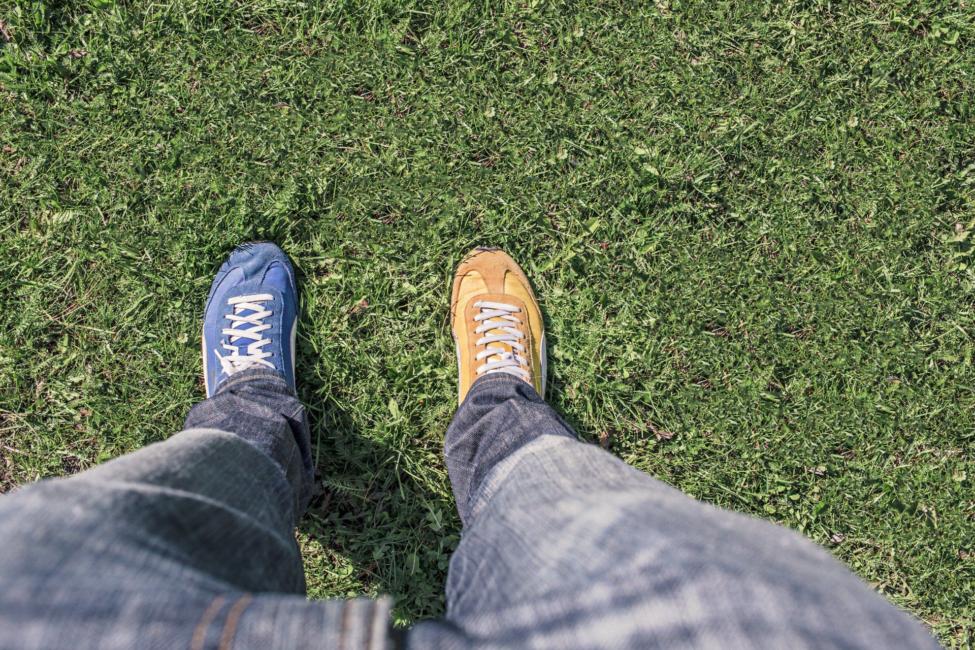 A person is standing in the grass wearing different shoes.