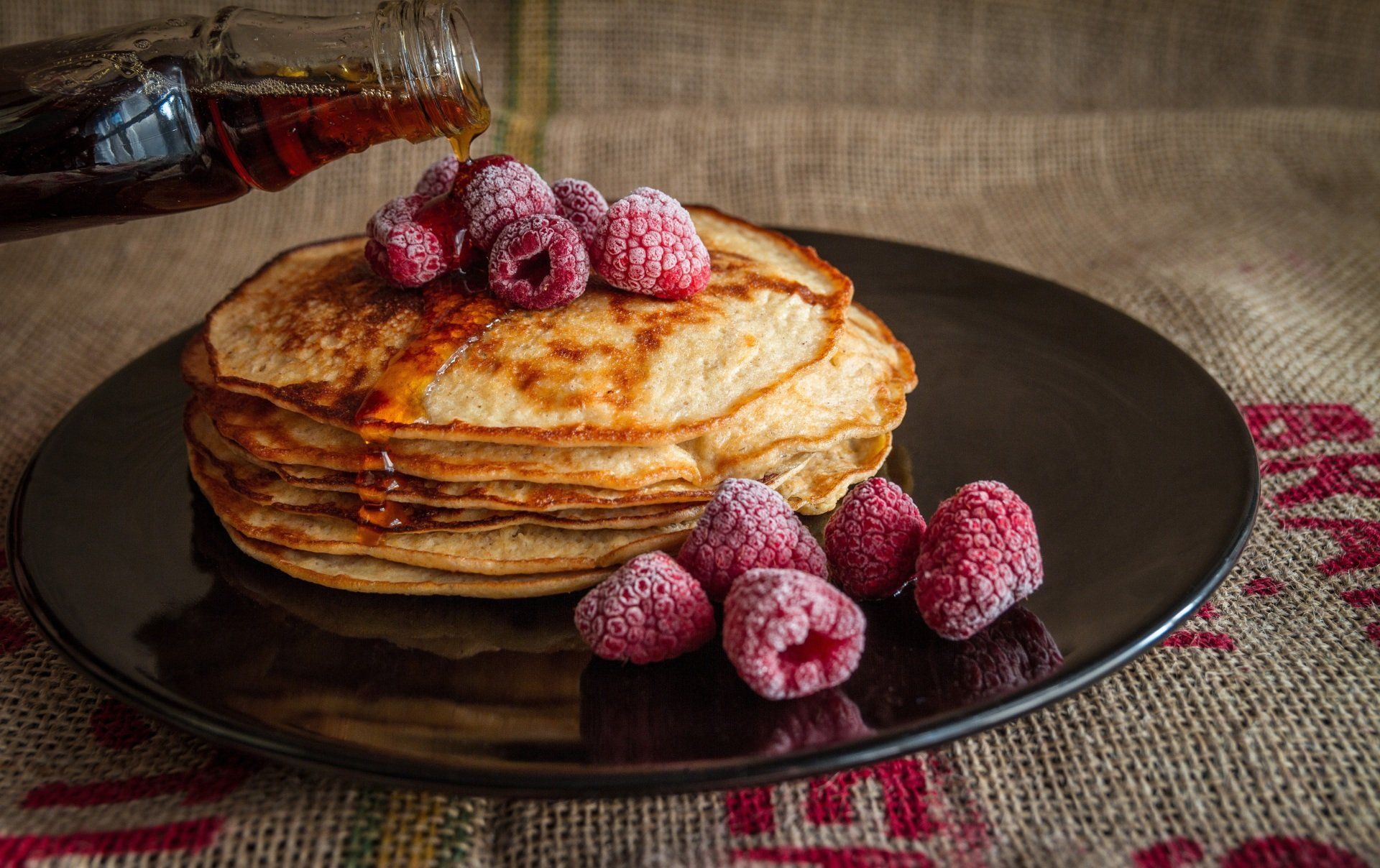A stack of pancakes with raspberries and wholesale pure maple syrup.