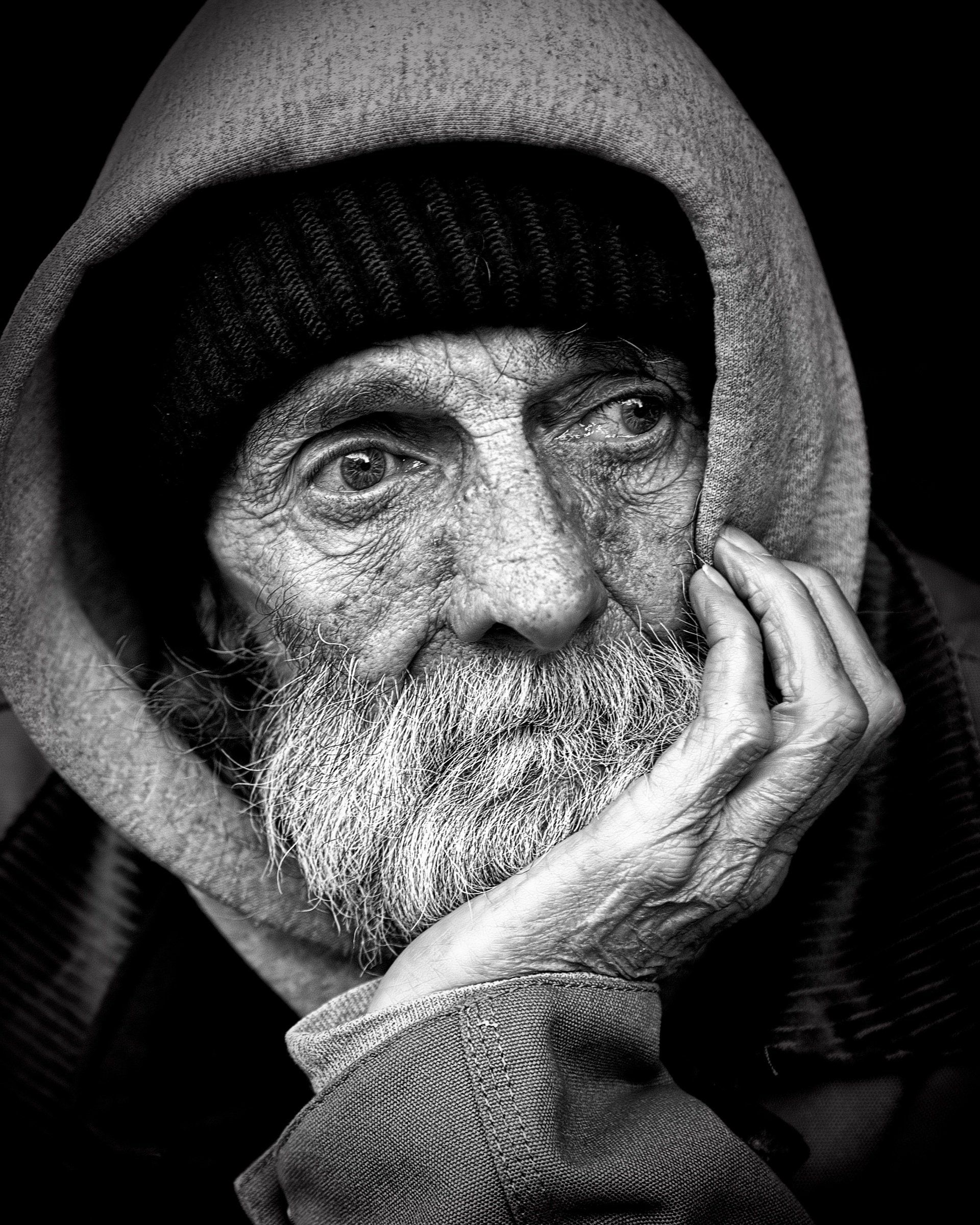 Uma foto em preto e branco de um velho com barba vestindo uma jaqueta com capuz.