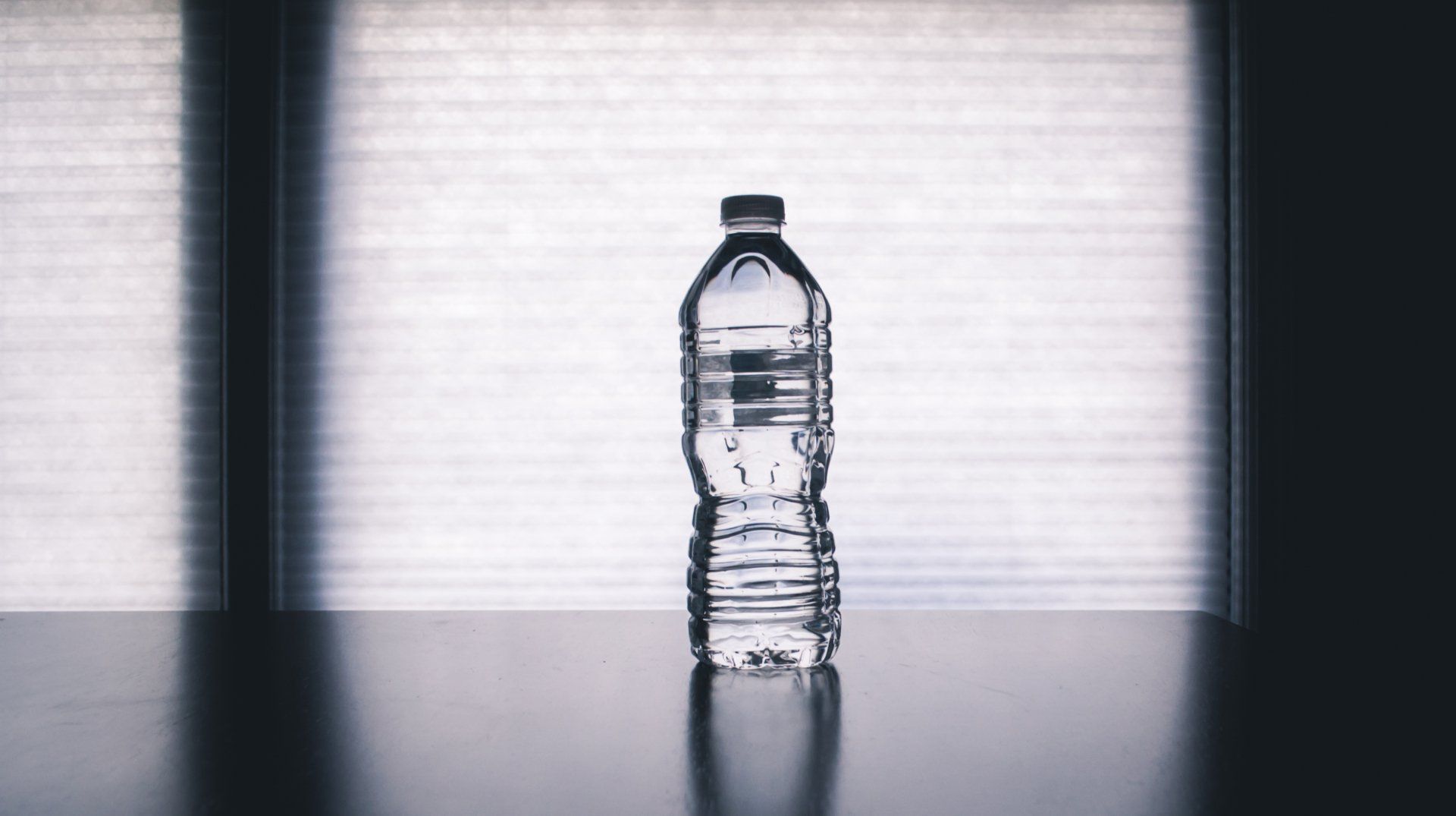 A bottle of water is sitting on a table in front of a window.