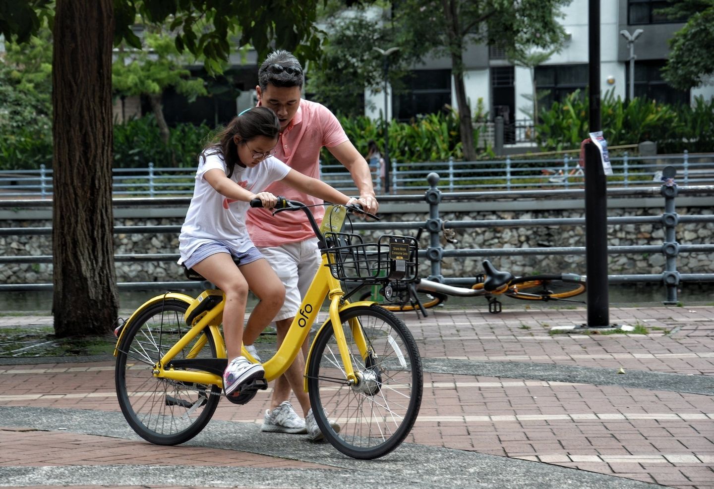 A man is teaching a little girl how to ride a bike.