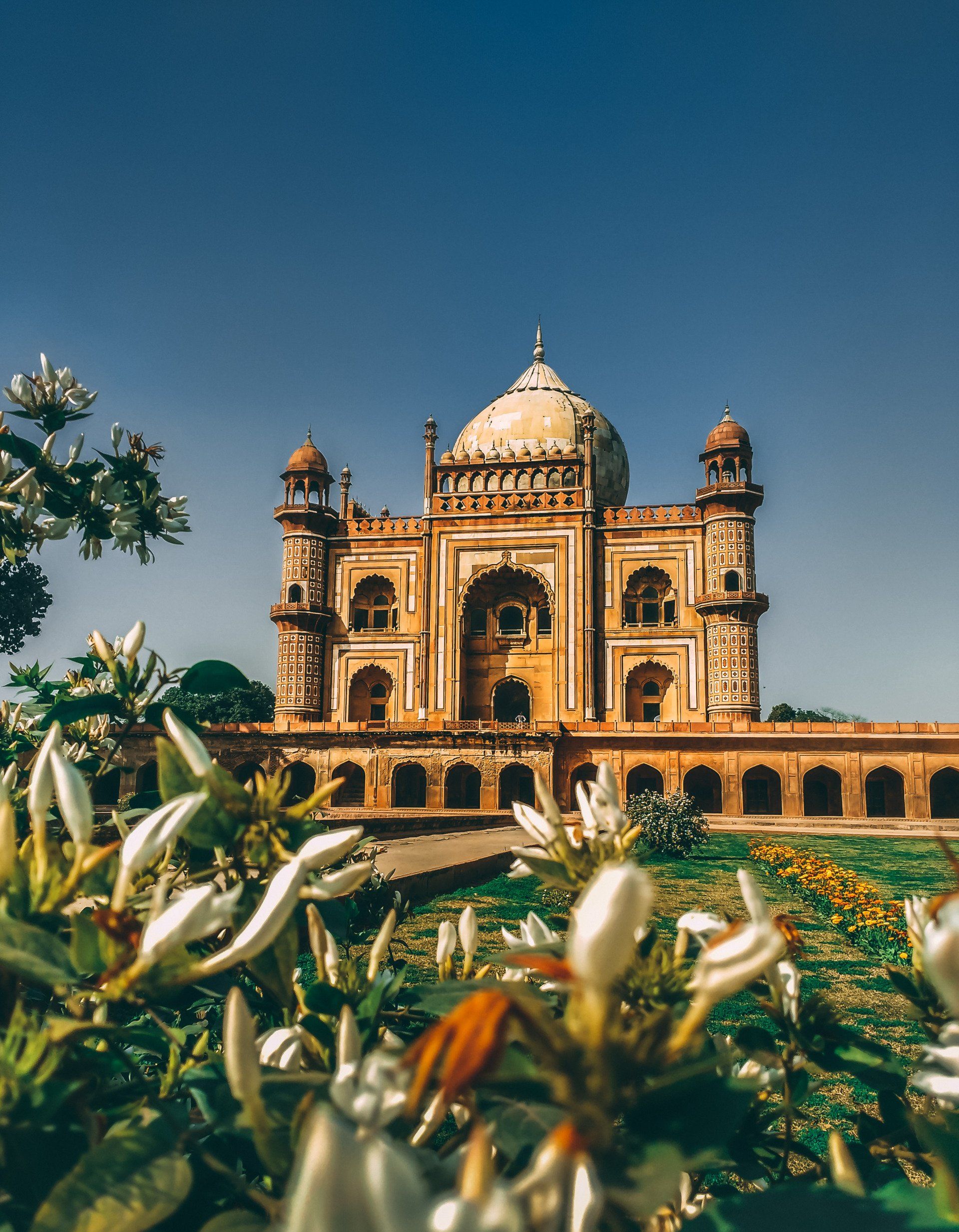 Safdarjung Tomb, New Delhi, India. White dome and arched structure, floral foreground, bright blue sky.