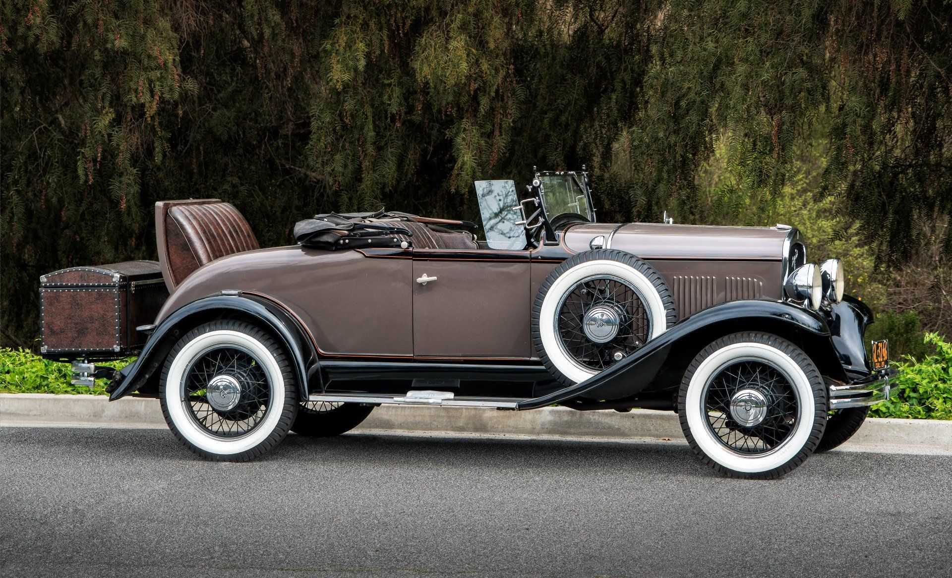 An old brown car with white tires is parked on the side of the road.