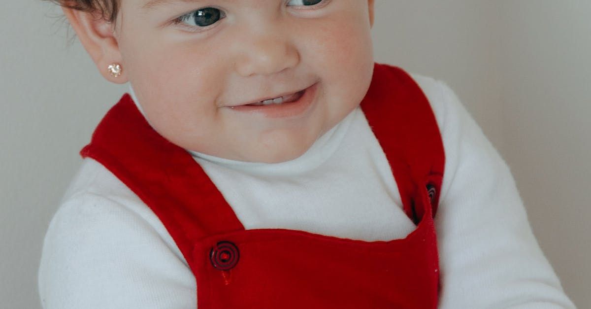 A little girl wearing red overalls and a white shirt is smiling.