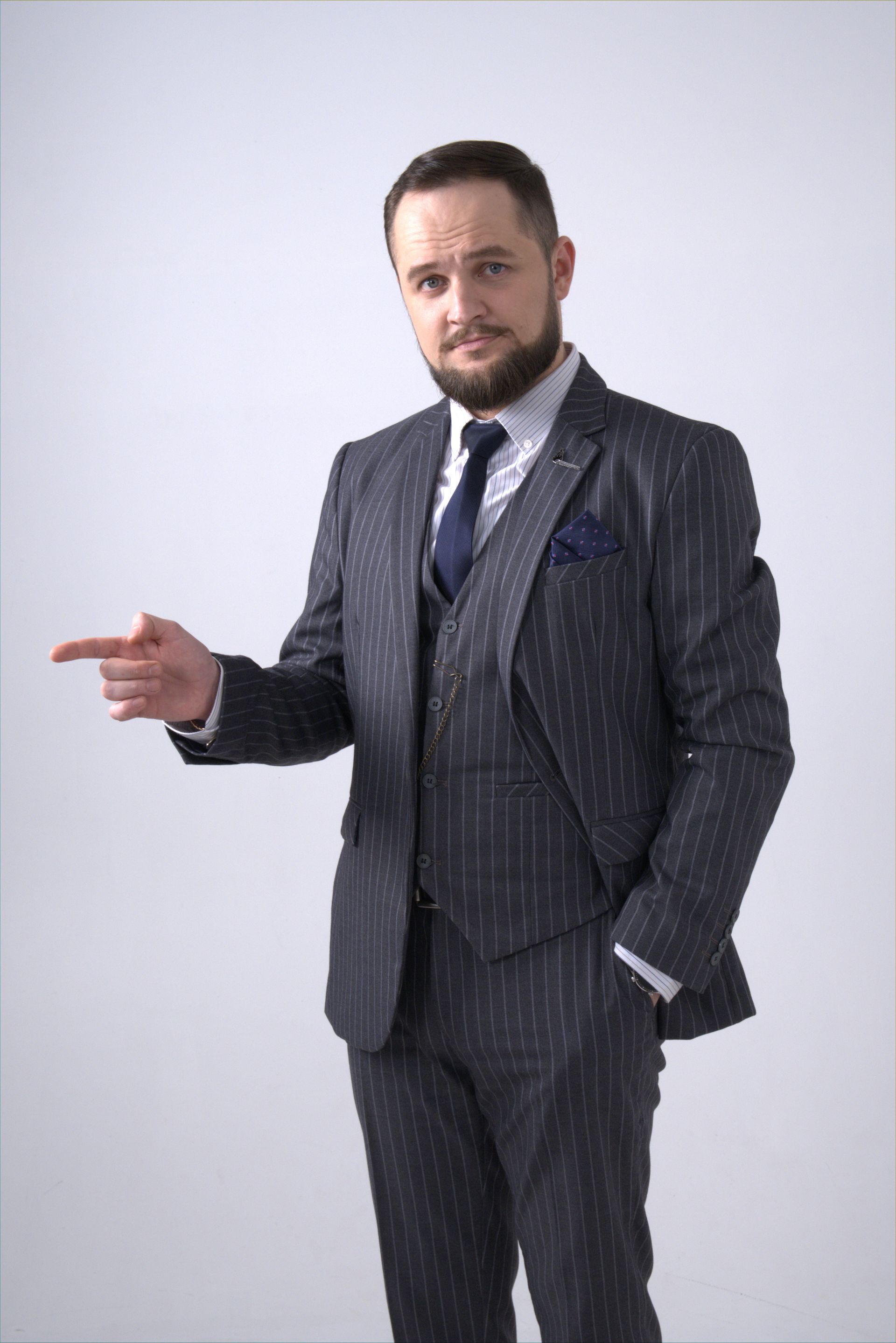 Man in pinstripe suit pointing left, looking at viewer. White background.