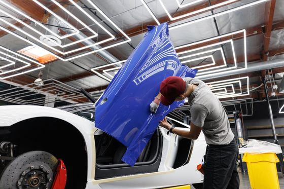 Man wrapping blue film on a white Lamborghini door in a brightly lit garage.