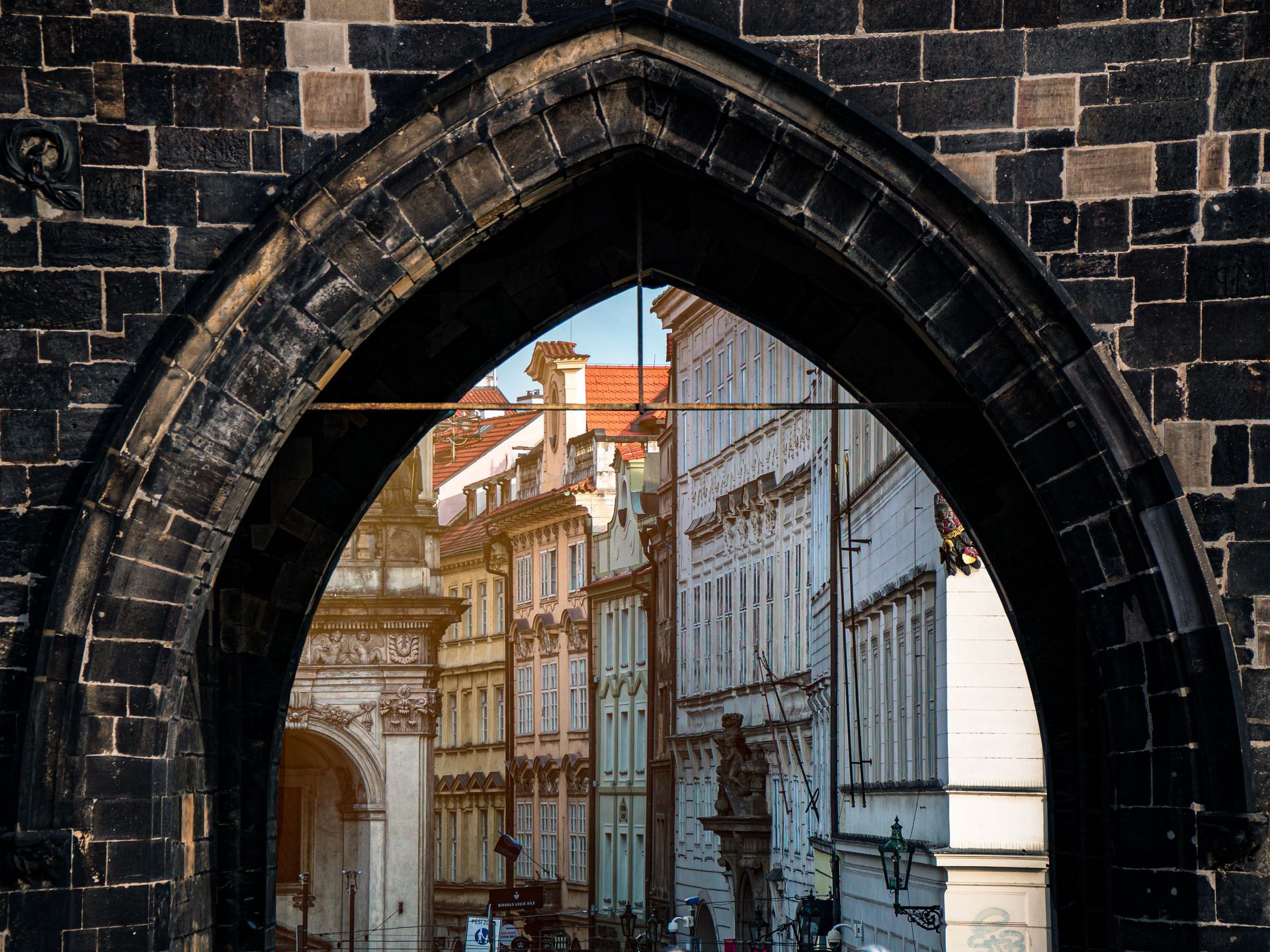 View through a stone archway to a narrow street of old buildings with white facades and red roofs.