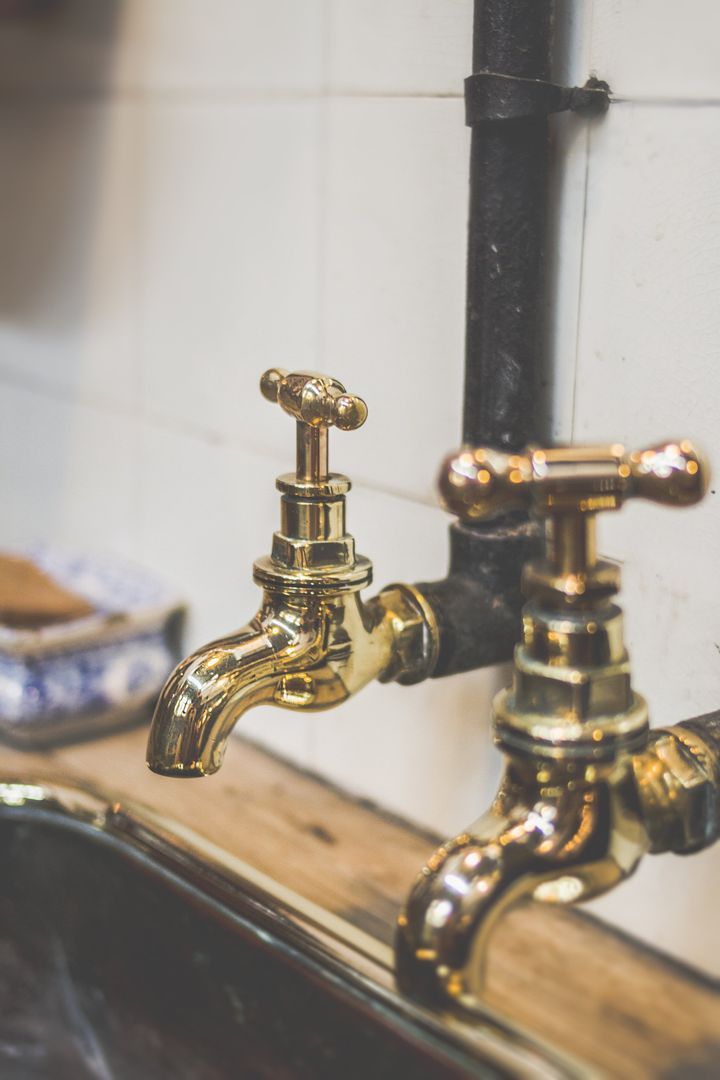 Industriële look van 2 gouden kranen met een zwart geverfde aansluitleiding in een wit betegelde keuken