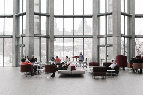 A group of people are sitting in a large room with a lot of windows.