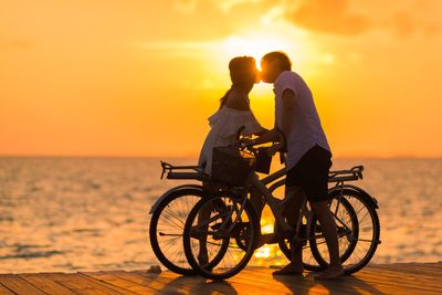 A man is holding a baby in his arms in front of a window while the sun is setting. 