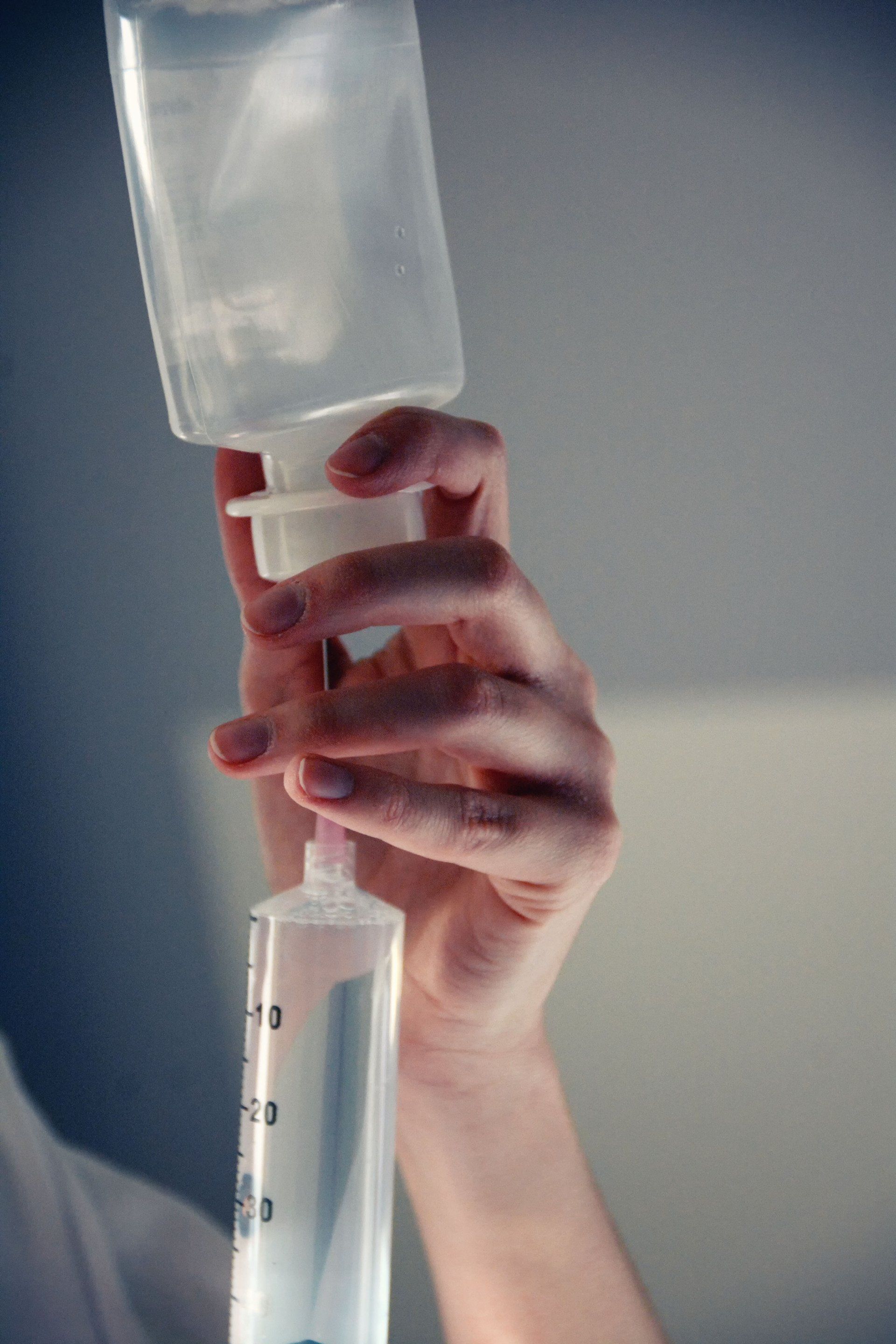 Hand holding and connecting an IV bag to an IV tube, preparing for fluid administration.