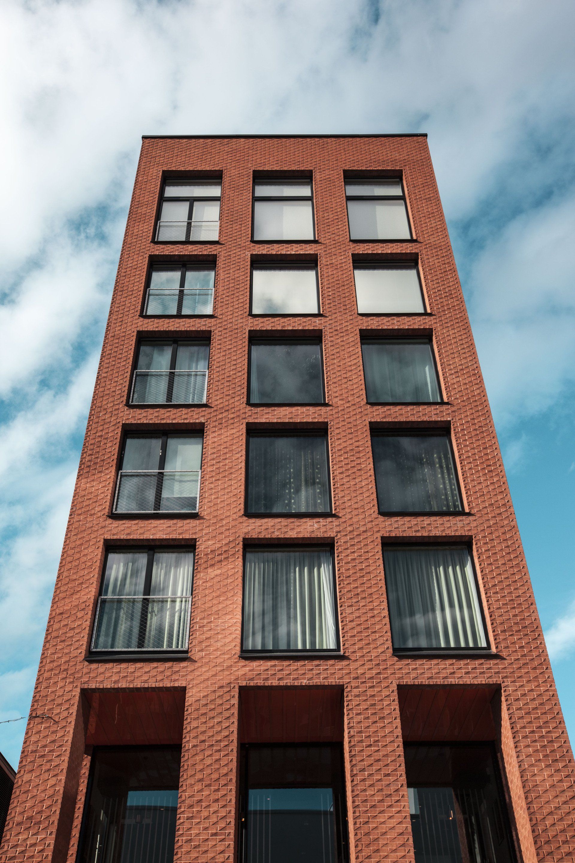 Tall red brick apartment building viewed from below against a cloudy sky
