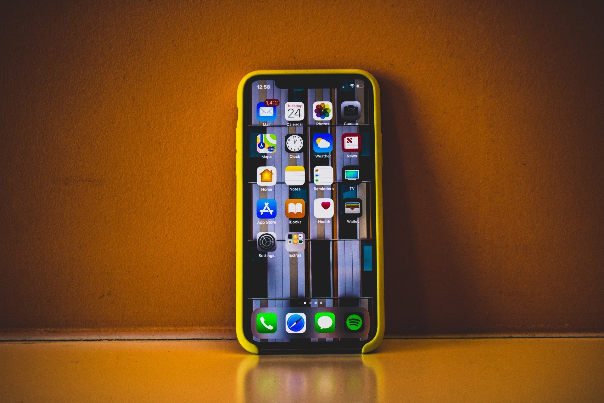 Smartphone with lit home screen standing on a shelf against a warm orange wall