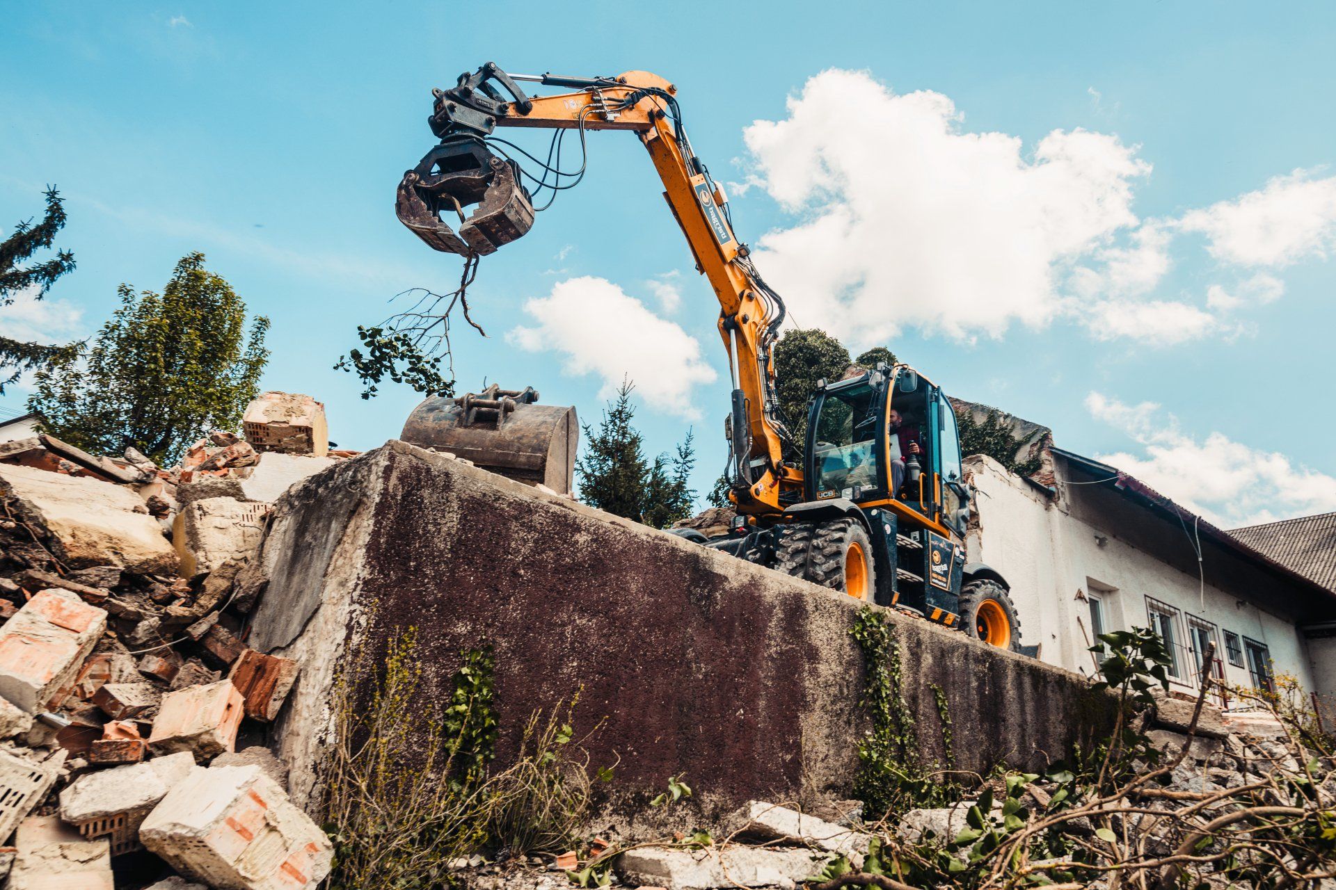 Excavator demolishing a concrete structure amid rubble under a blue sky