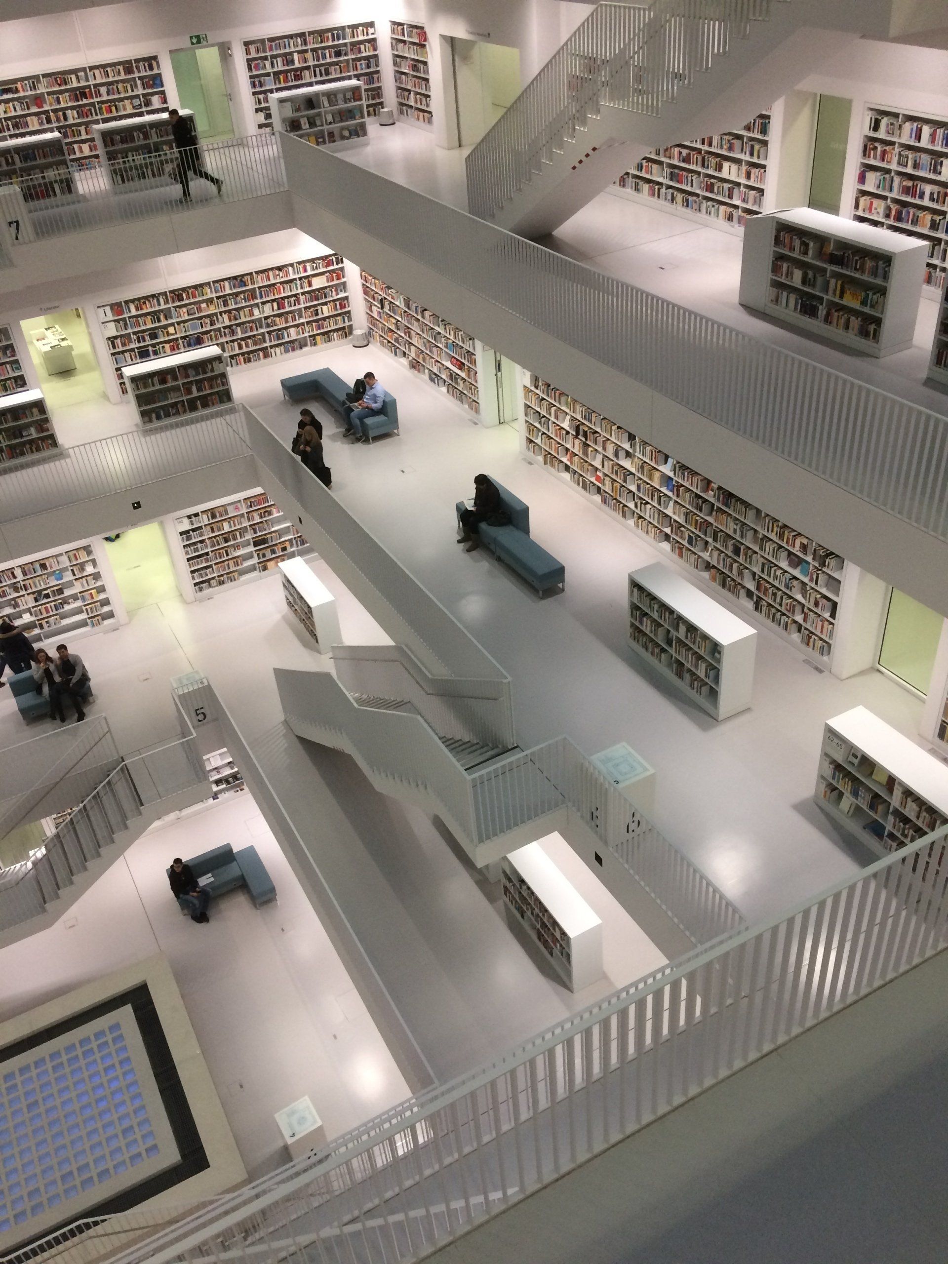 Multilevel library interior with bookshelves, white railings, stairs, and scattered seating areas