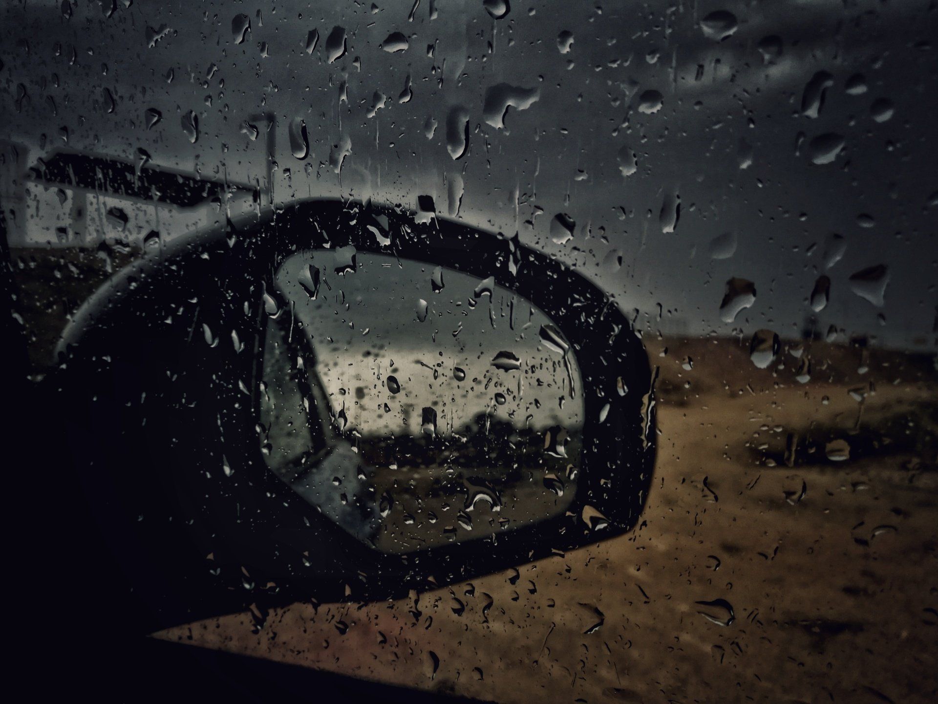 The rear view mirror of a car is covered in rain drops.