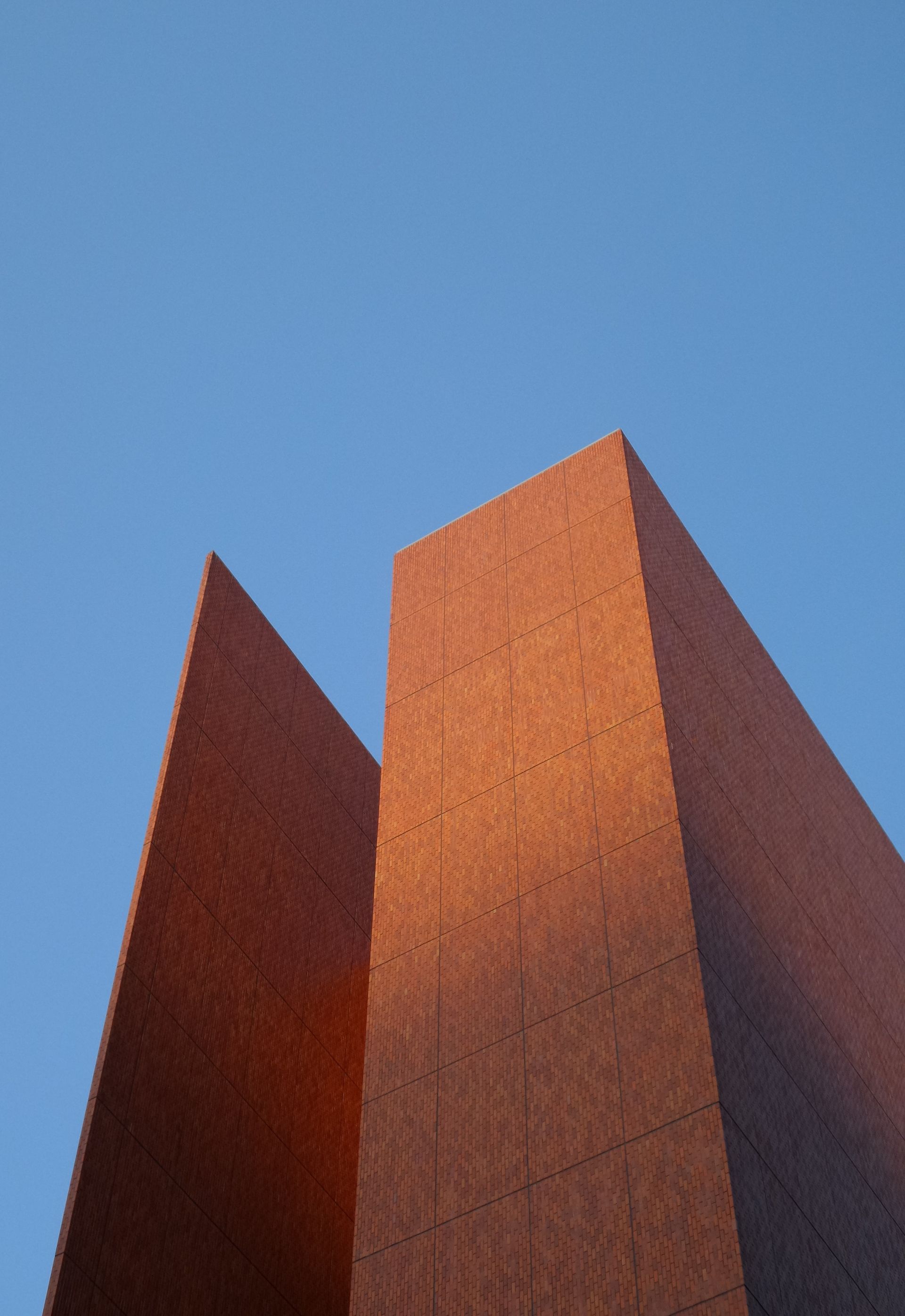 Brick building with angled facades, bathed in warm sunlight, against a blue sky.