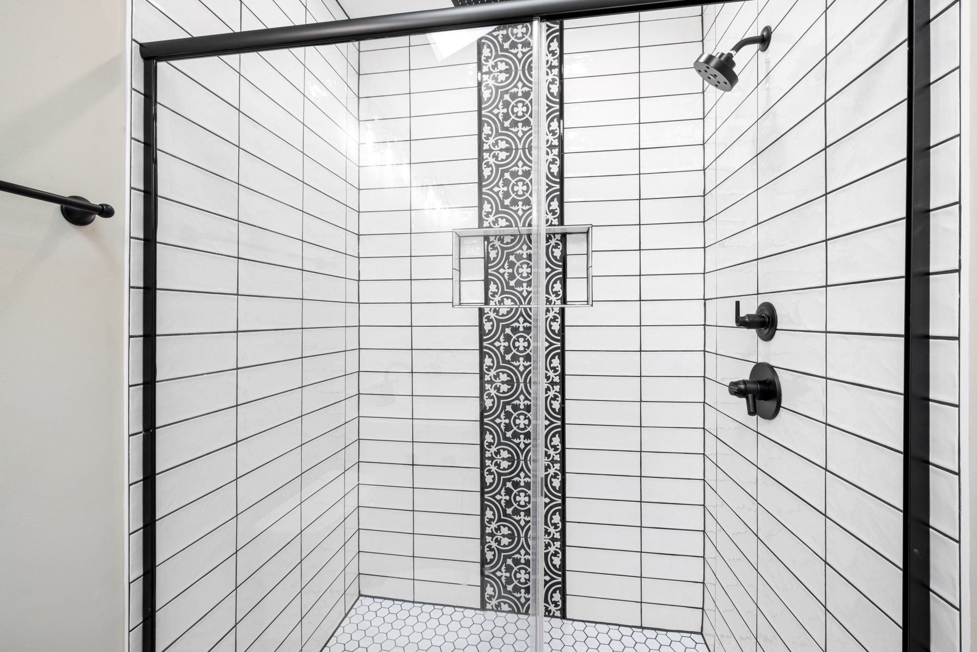 A bathroom with white tiles and a sliding glass shower door.