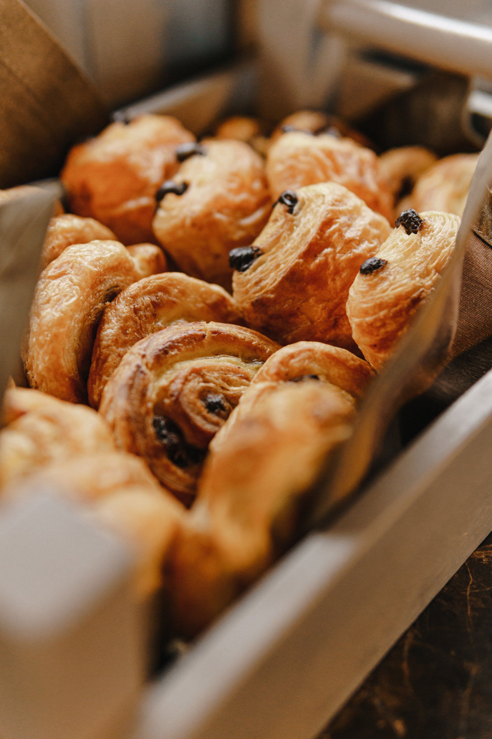 Box of assorted golden-brown pastries, including croissants and swirls, in a bakery display.