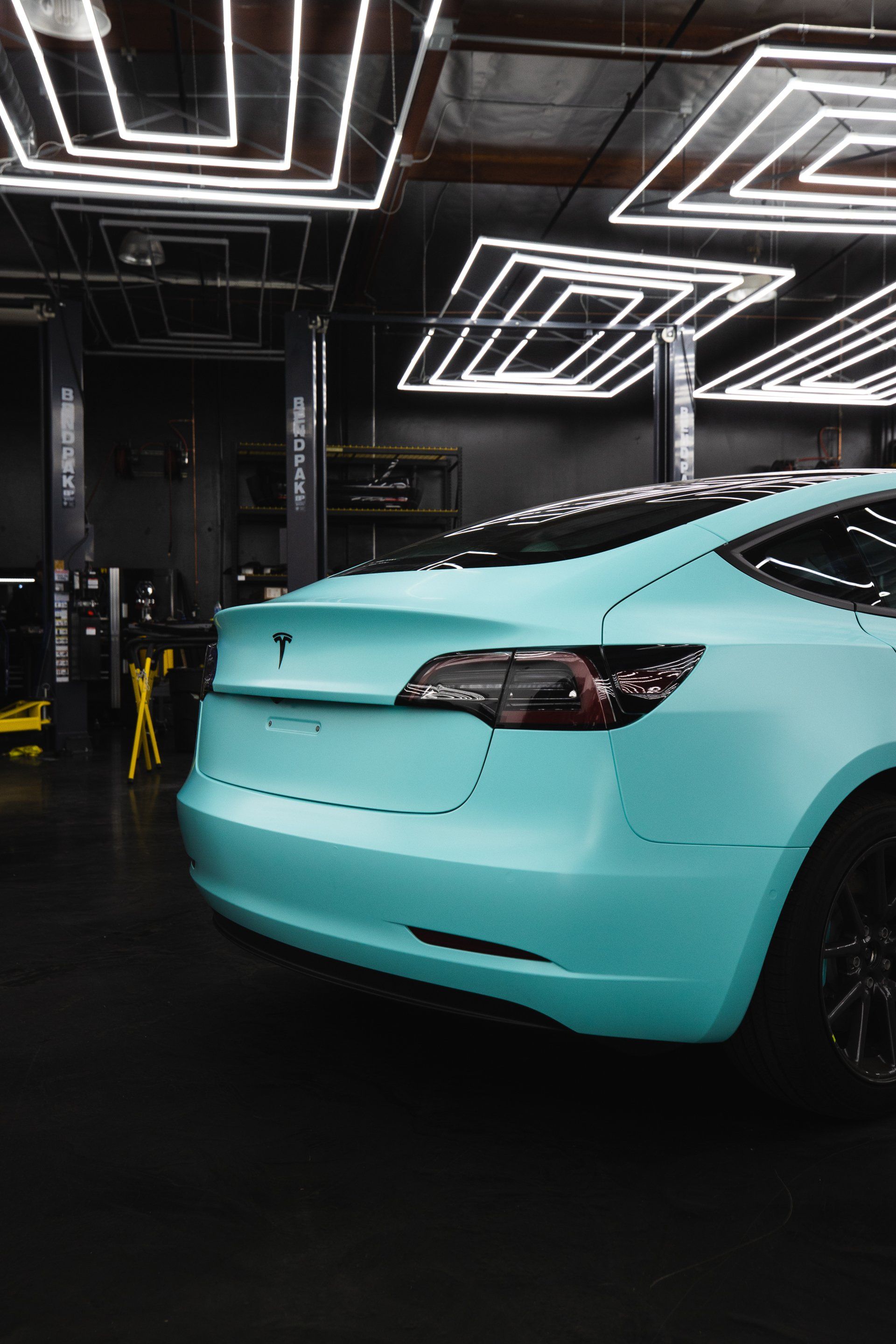 A blue tesla model 3 is parked in a garage.