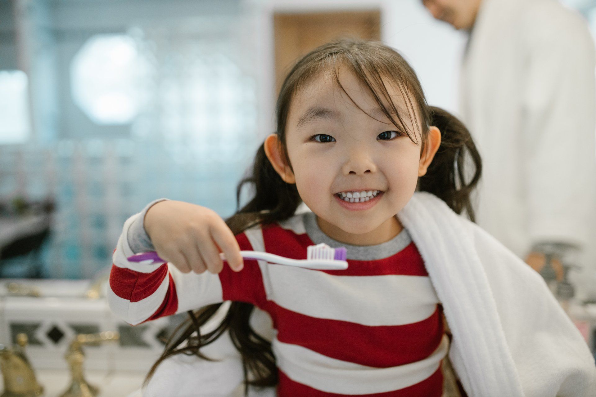 Girl smiling, holding toothbrush, getting ready to brush teeth in bathroom.