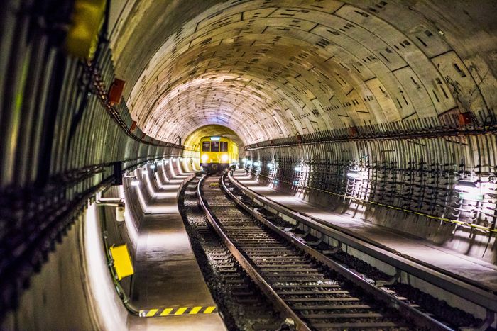 Subway tunnel with tracks leading toward a bright yellow train in the distance.