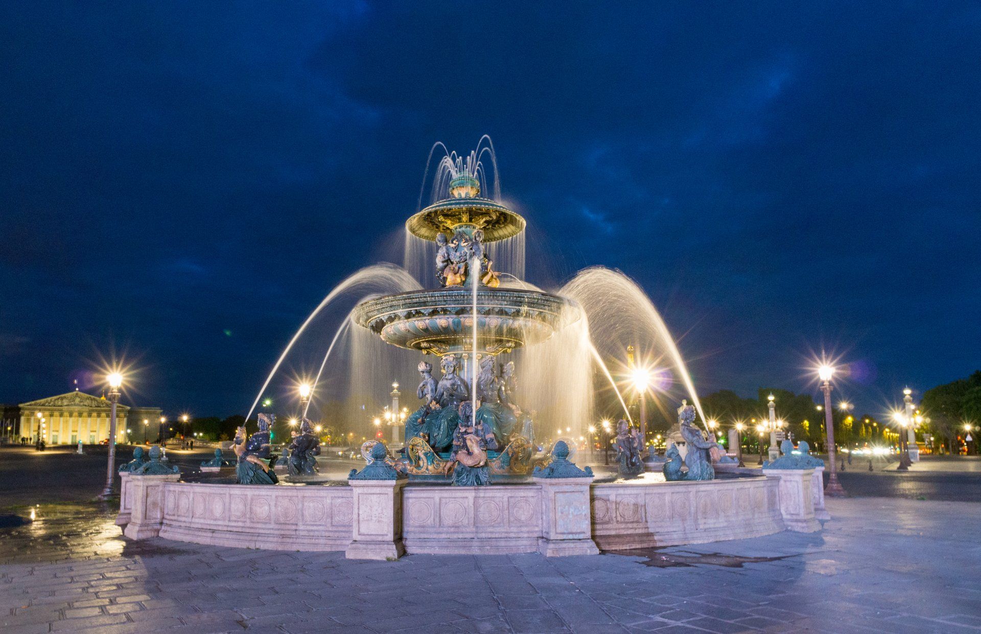 A large fountain is lit up at night in a park.