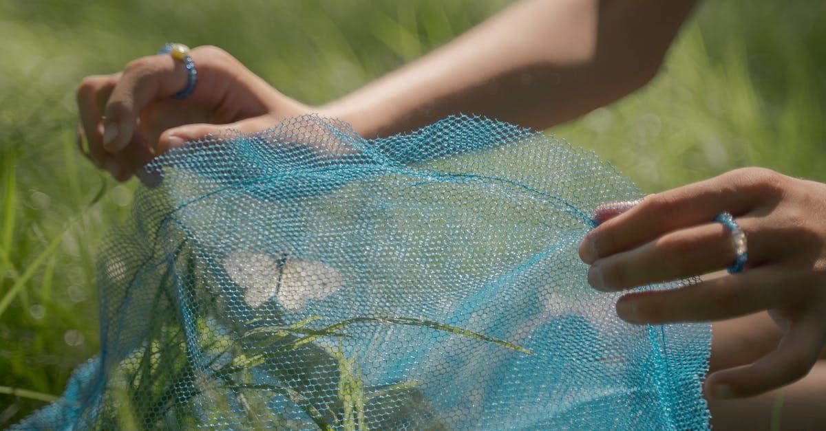 Person holding shimmering blue fabric outdoors, rings on fingers.