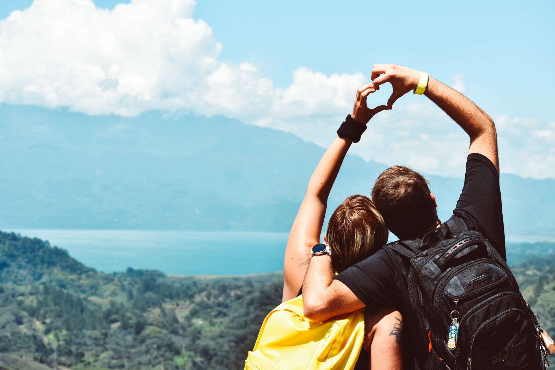 White couple sitting on top of a mountain holding hands in the shape of a love heart.