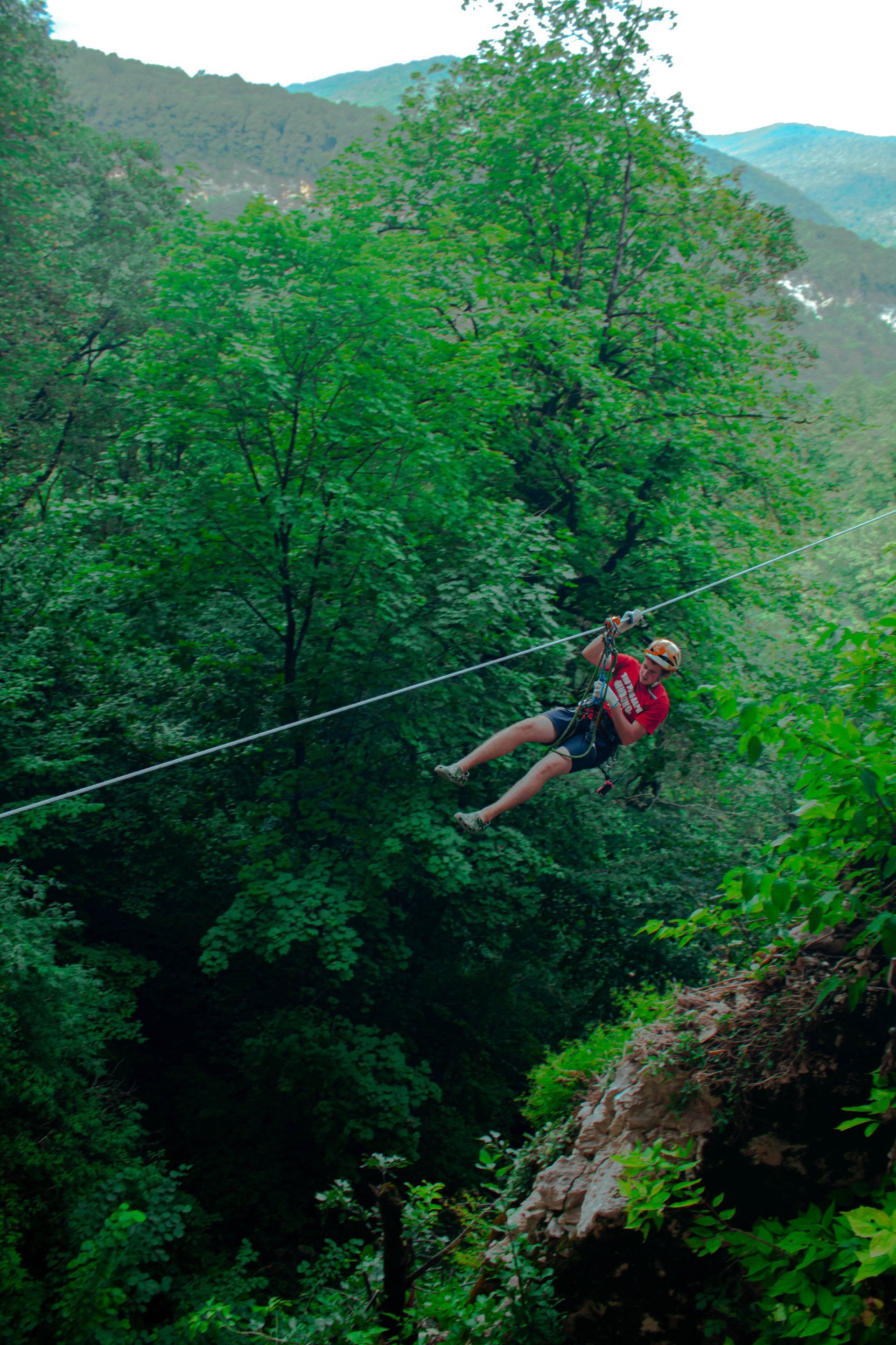 A man is flying through the air on a zip line in the woods.