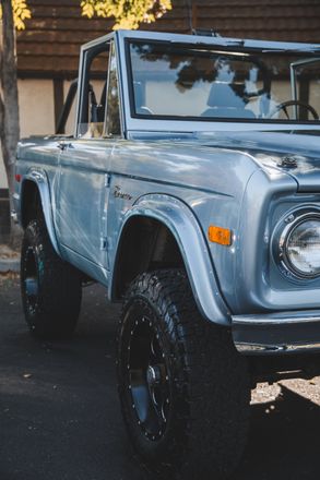 A blue ford bronco is parked on the side of the road.