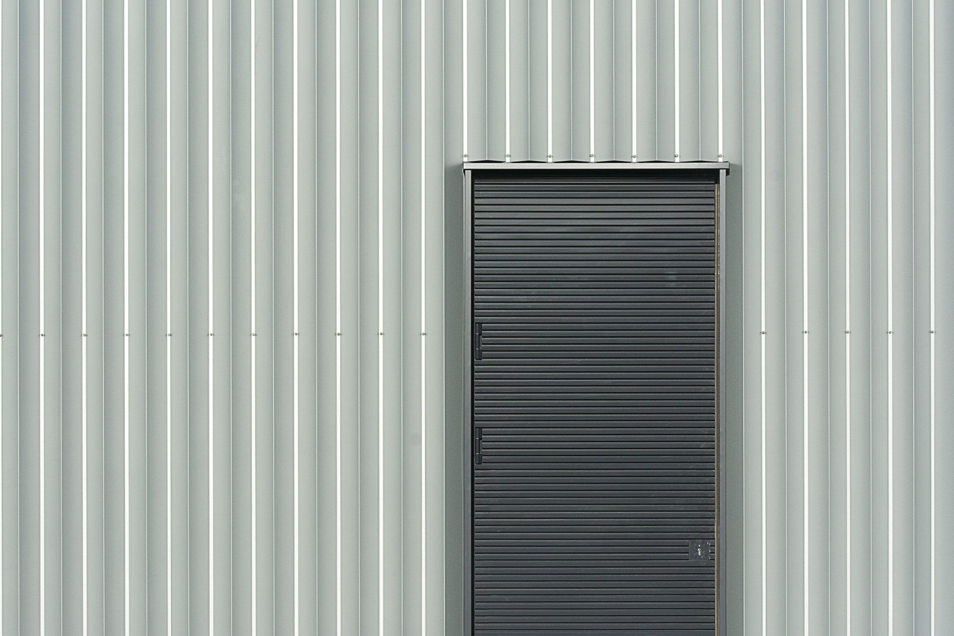 A black door is against a white corrugated metal wall.
