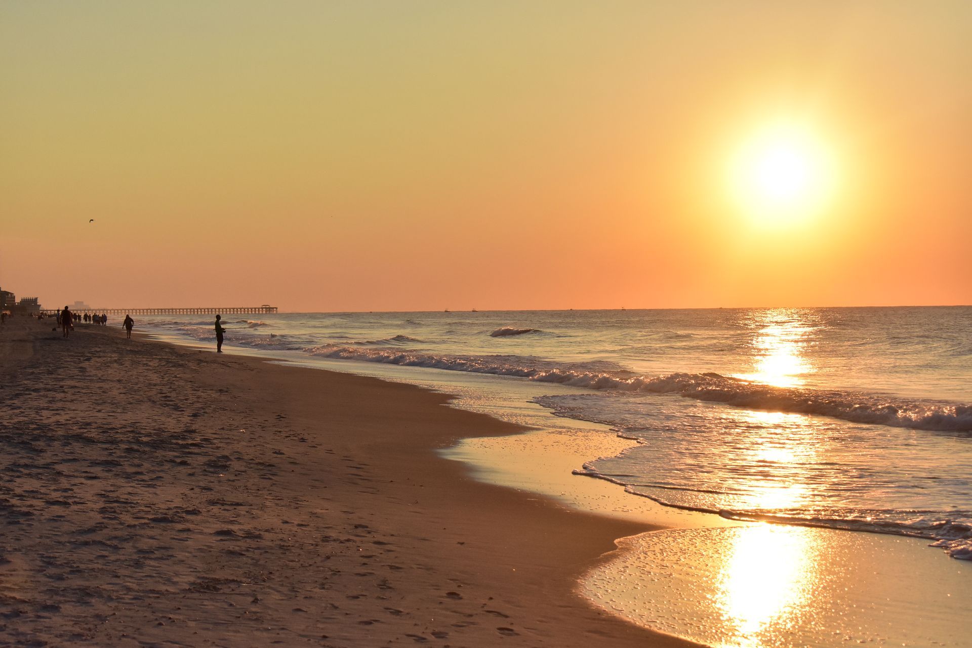 Sunset over a calm beach with waves washing ashore and golden light reflecting on the water