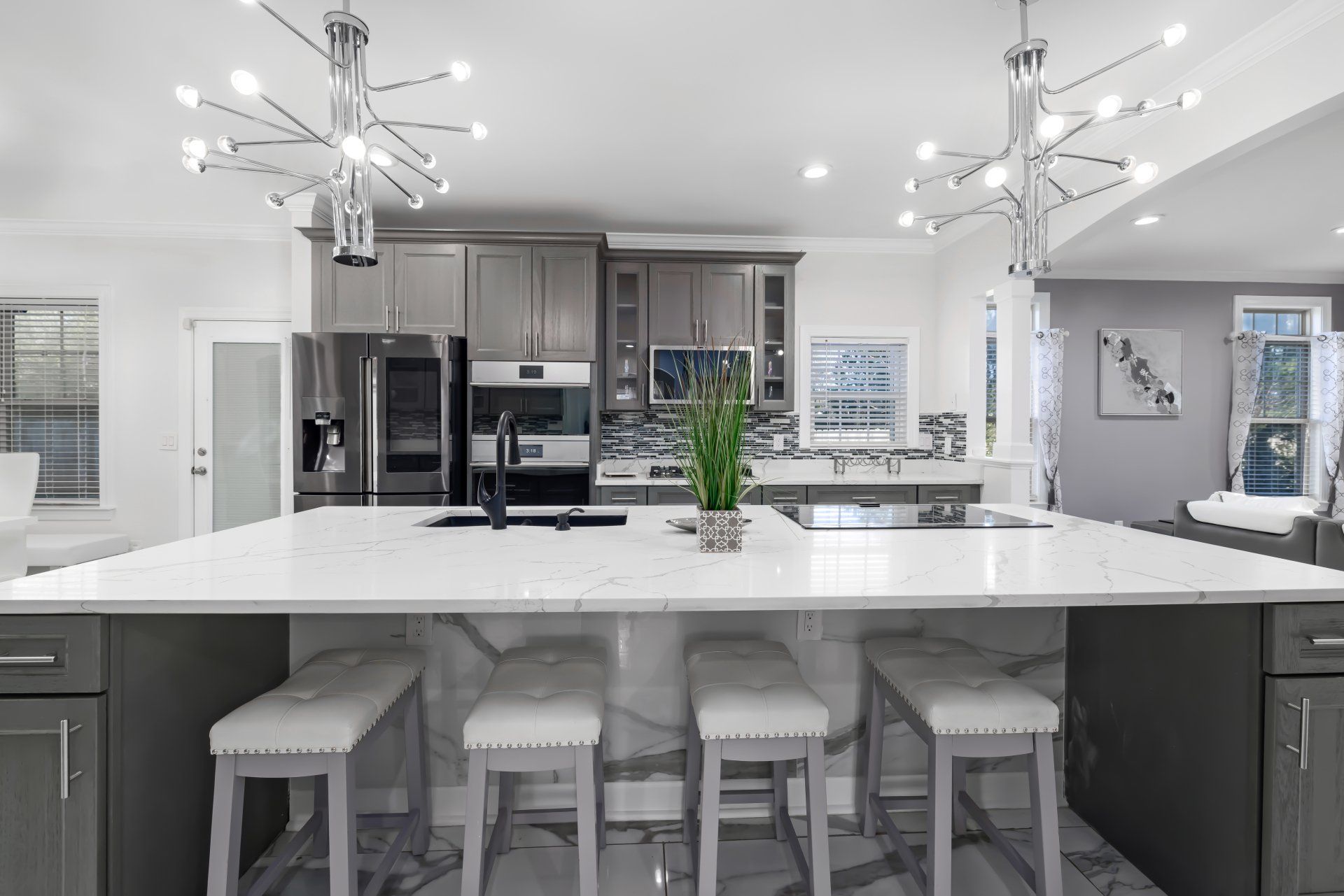 Bright modern kitchen with white island, stools, pendant lights, and stainless steel appliances