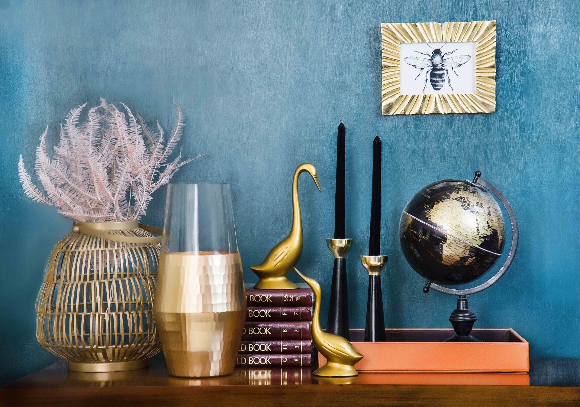 Decorative shelf with vase, candles, globe, gold swan, and framed bee against a blue wall