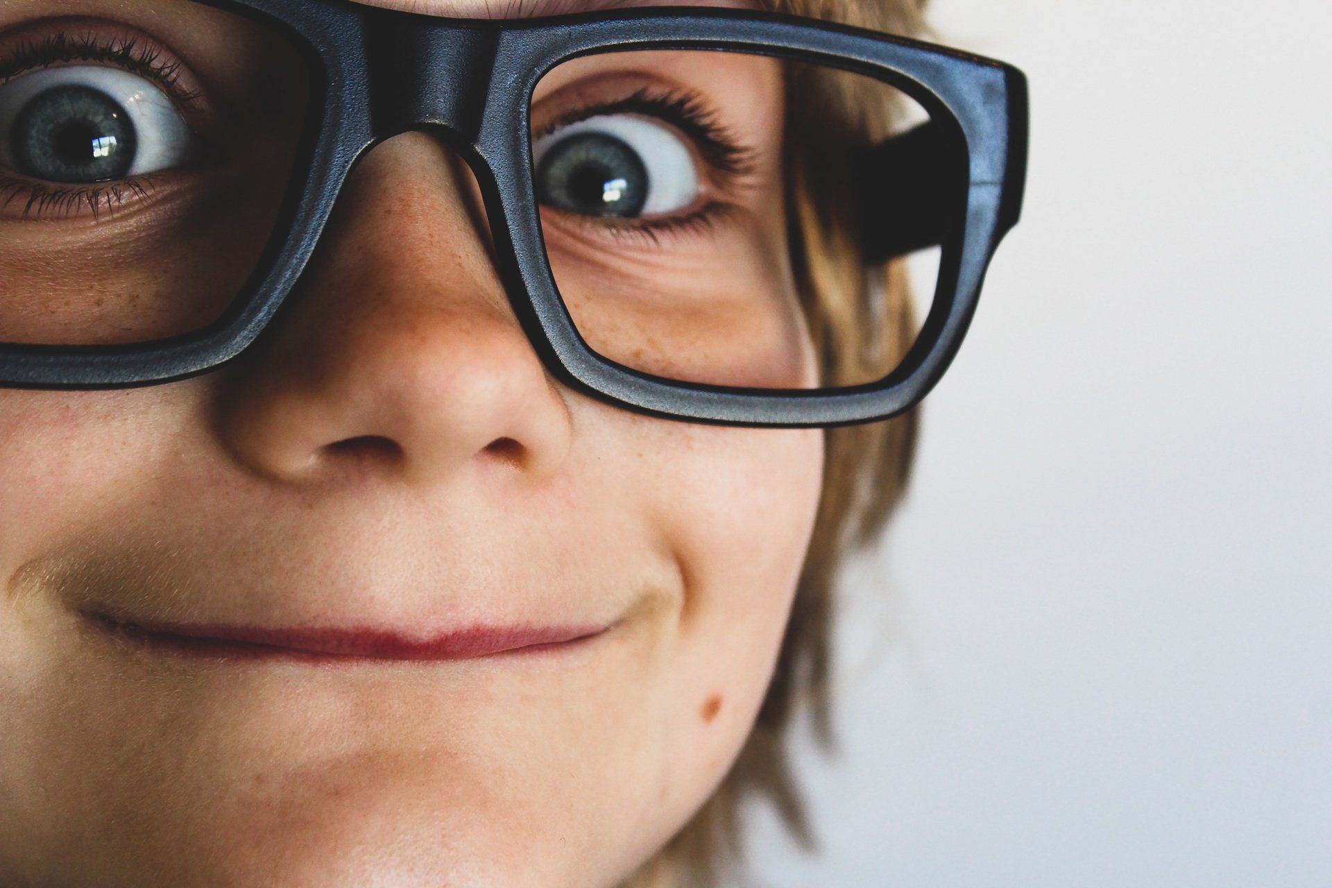 Gros plan d'une personne souriante portant de grandes lunettes noires sur fond clair