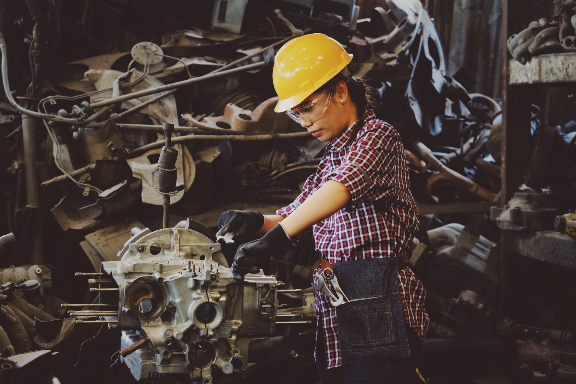 A man wearing a hard hat and safety glasses is working on a machine.