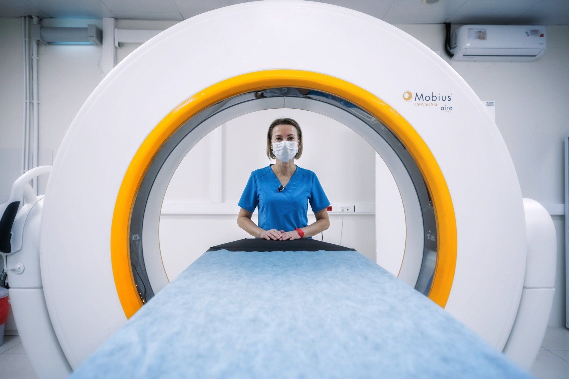 A nurse wearing a mask is standing in front of a ct scan machine.