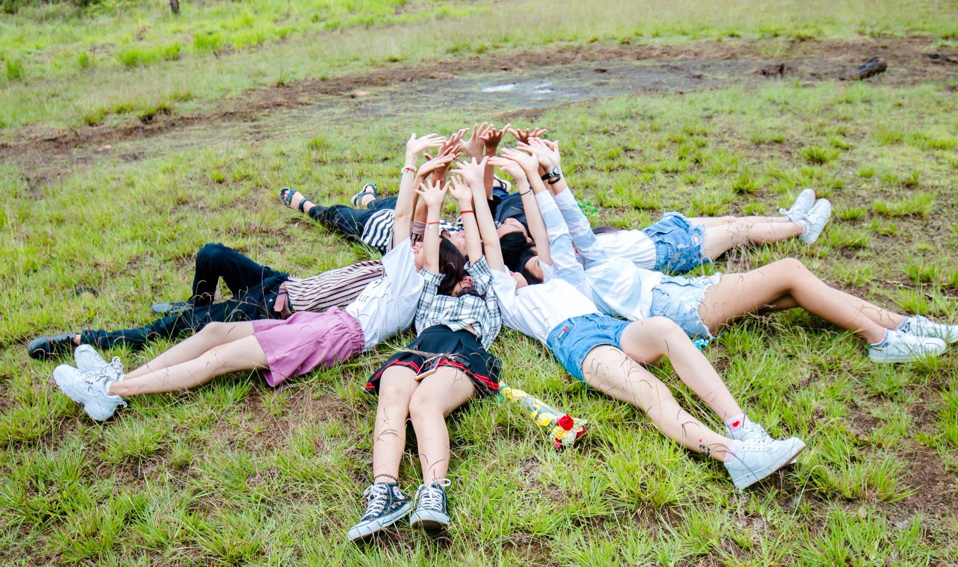 People lying on grass in star shape with arms raised.